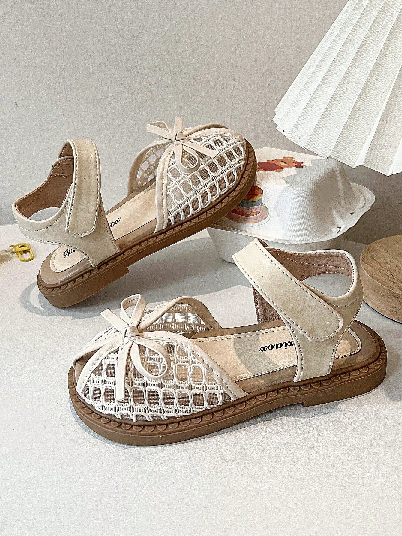 Pair of girls' pink open-toe flat sandals with ankle straps, buckle details, and a non-slip black rubber outsole.