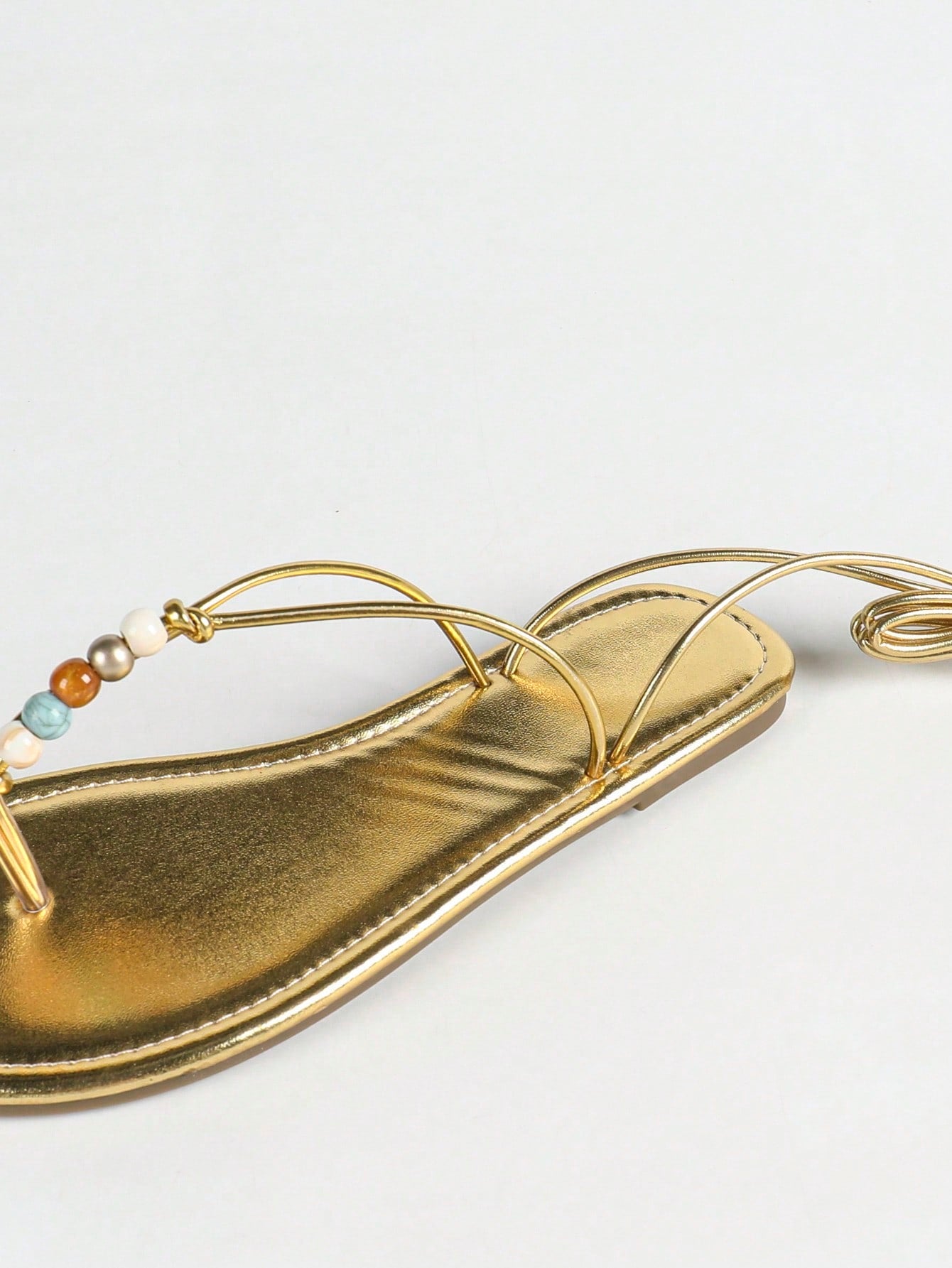 Women's gold flat sandals with metal accent detail, strappy lace-up design, and toe post thong style.