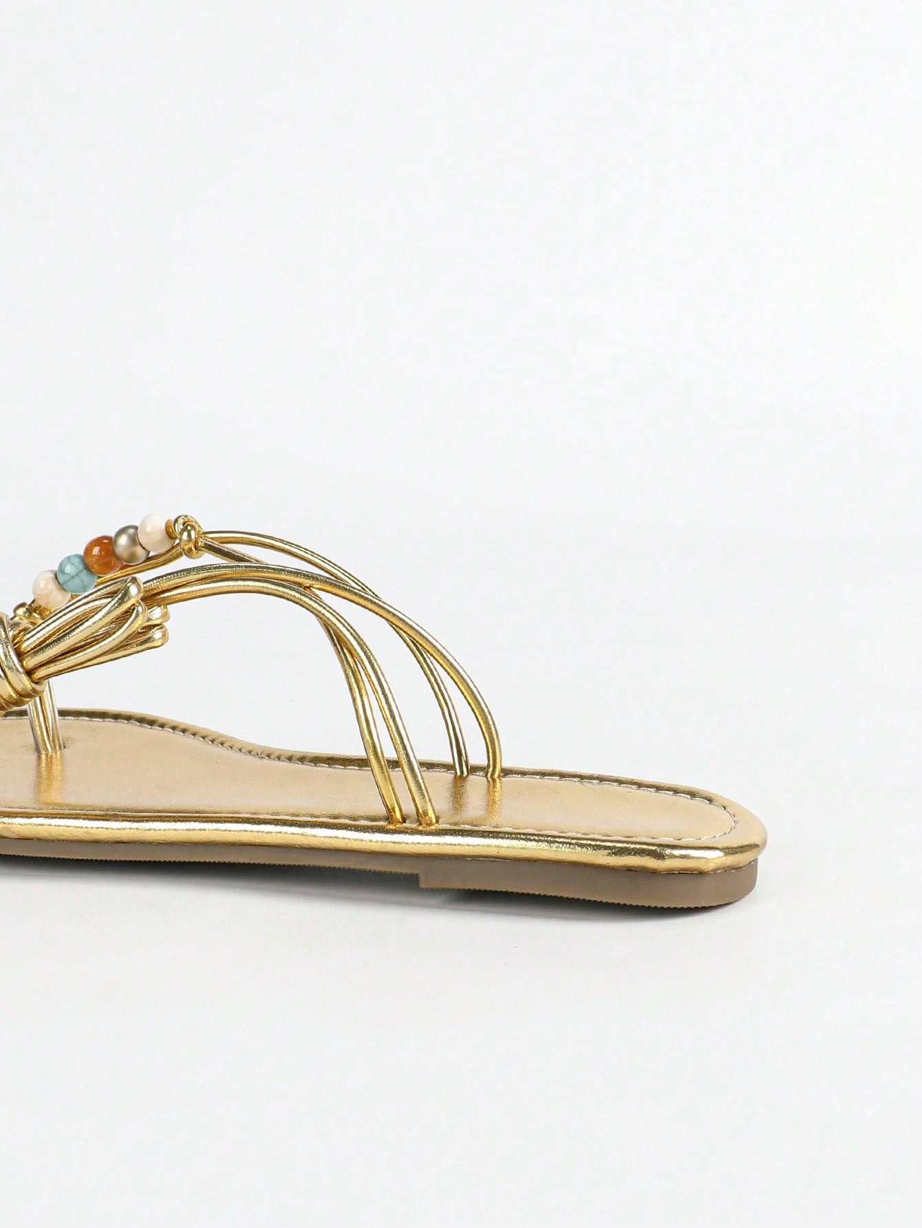 Women's gold flat sandals with metal accent detail, strappy lace-up design, and toe post thong style.