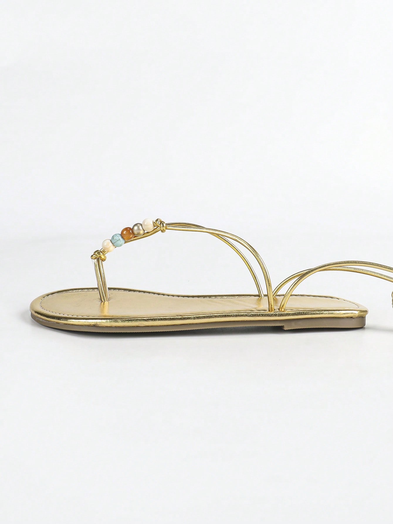 Women's gold flat sandals with metal accent detail, strappy lace-up design, and toe post thong style.