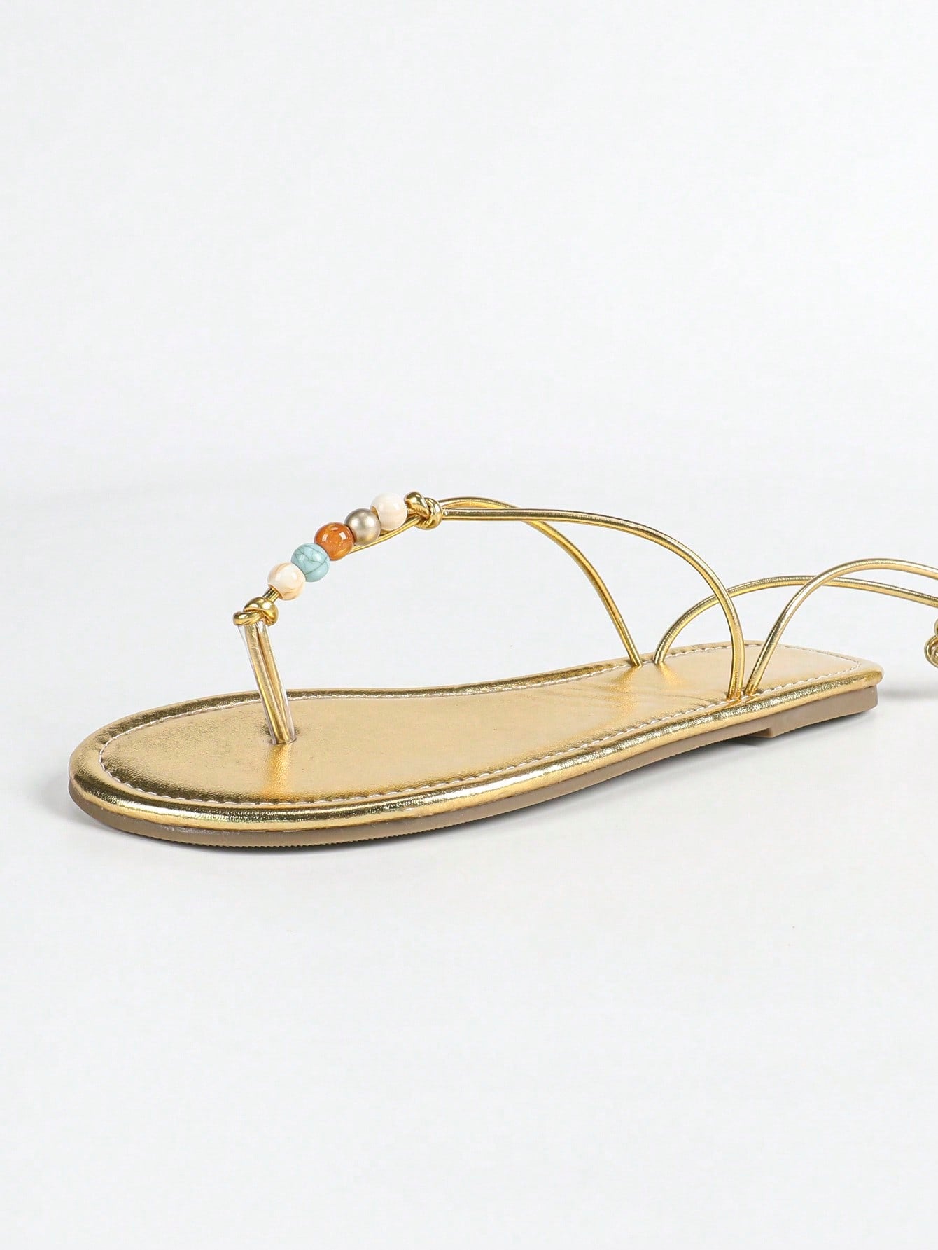 Women's gold flat sandals with metal accent detail, strappy lace-up design, and toe post thong style.