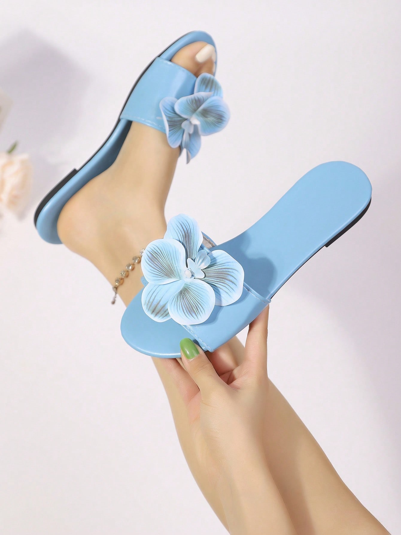 Women’s open toe flat toe-ring slide sandals with artificial flower applique detail and vacation beach style.