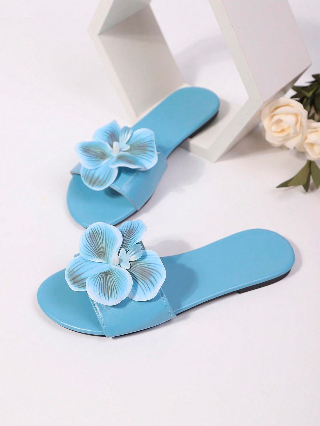 Women’s open toe flat toe-ring slide sandals with artificial flower applique detail and vacation beach style.