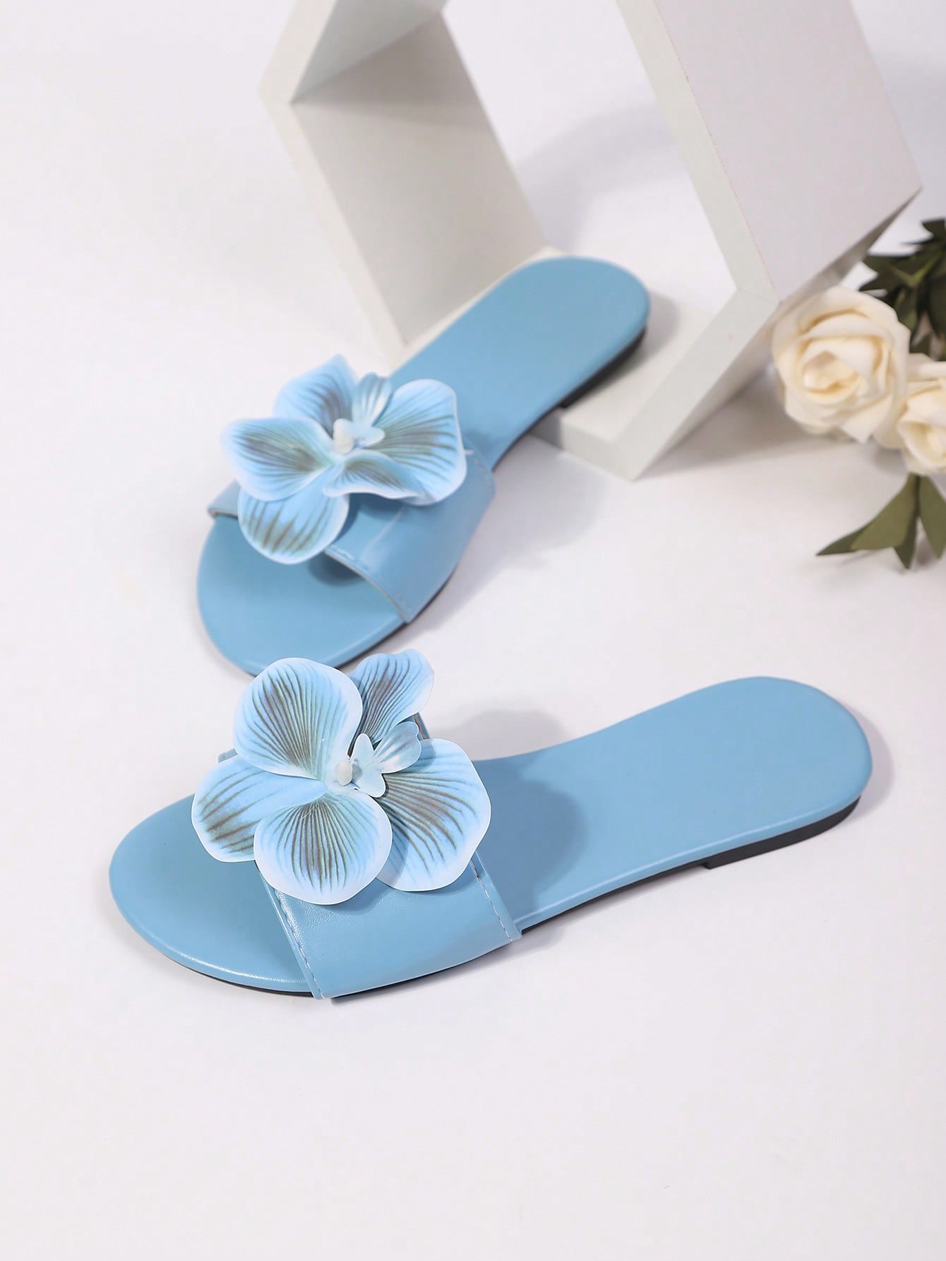 Women’s open toe flat toe-ring slide sandals with artificial flower applique detail and vacation beach style.