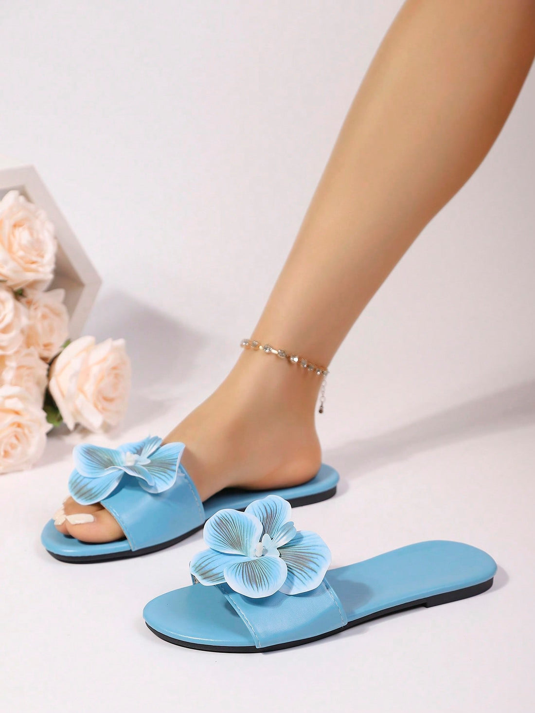 Women’s open toe flat toe-ring slide sandals with artificial flower applique detail and vacation beach style.