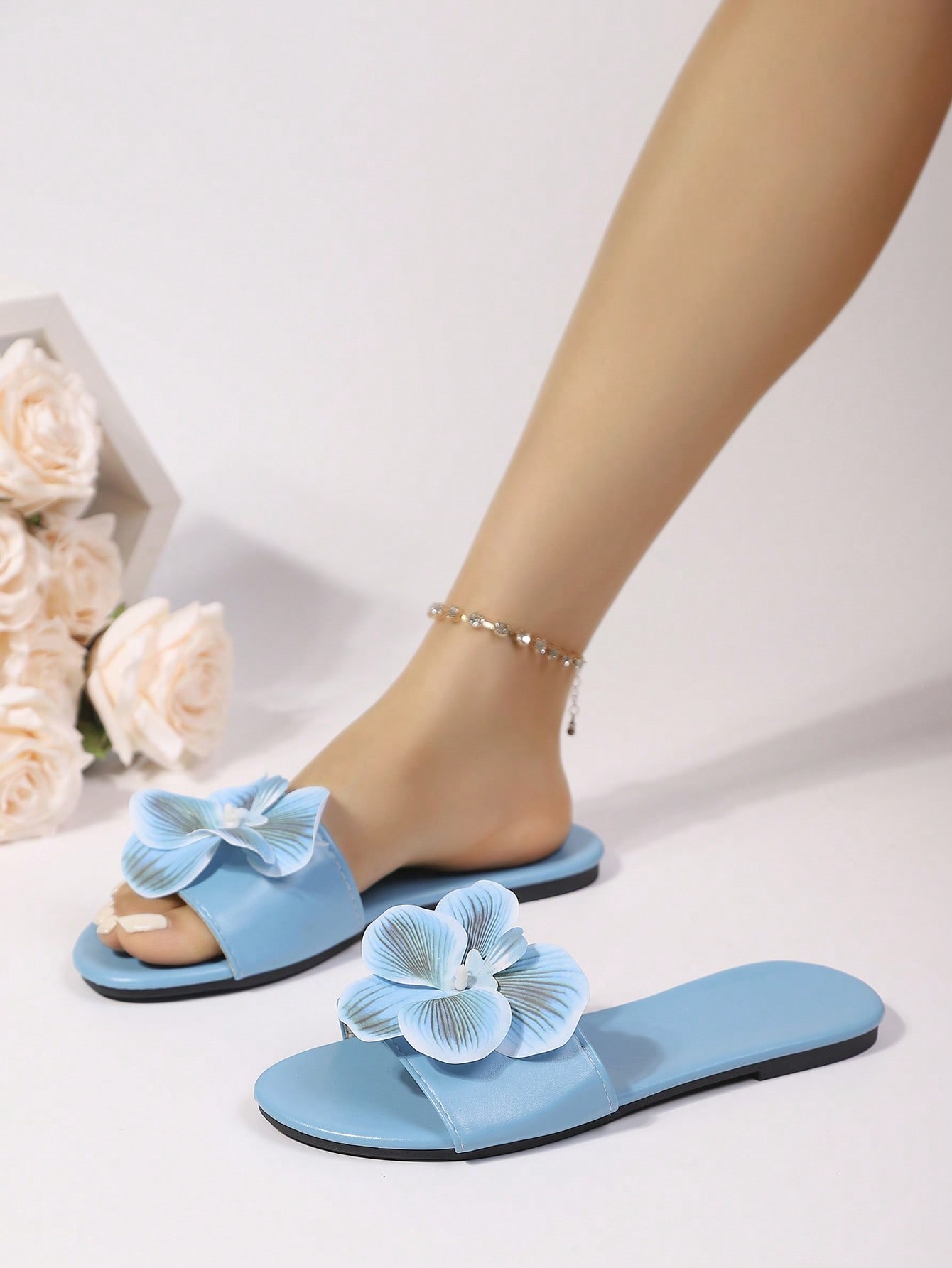 Women’s open toe flat toe-ring slide sandals with artificial flower applique detail and vacation beach style.
