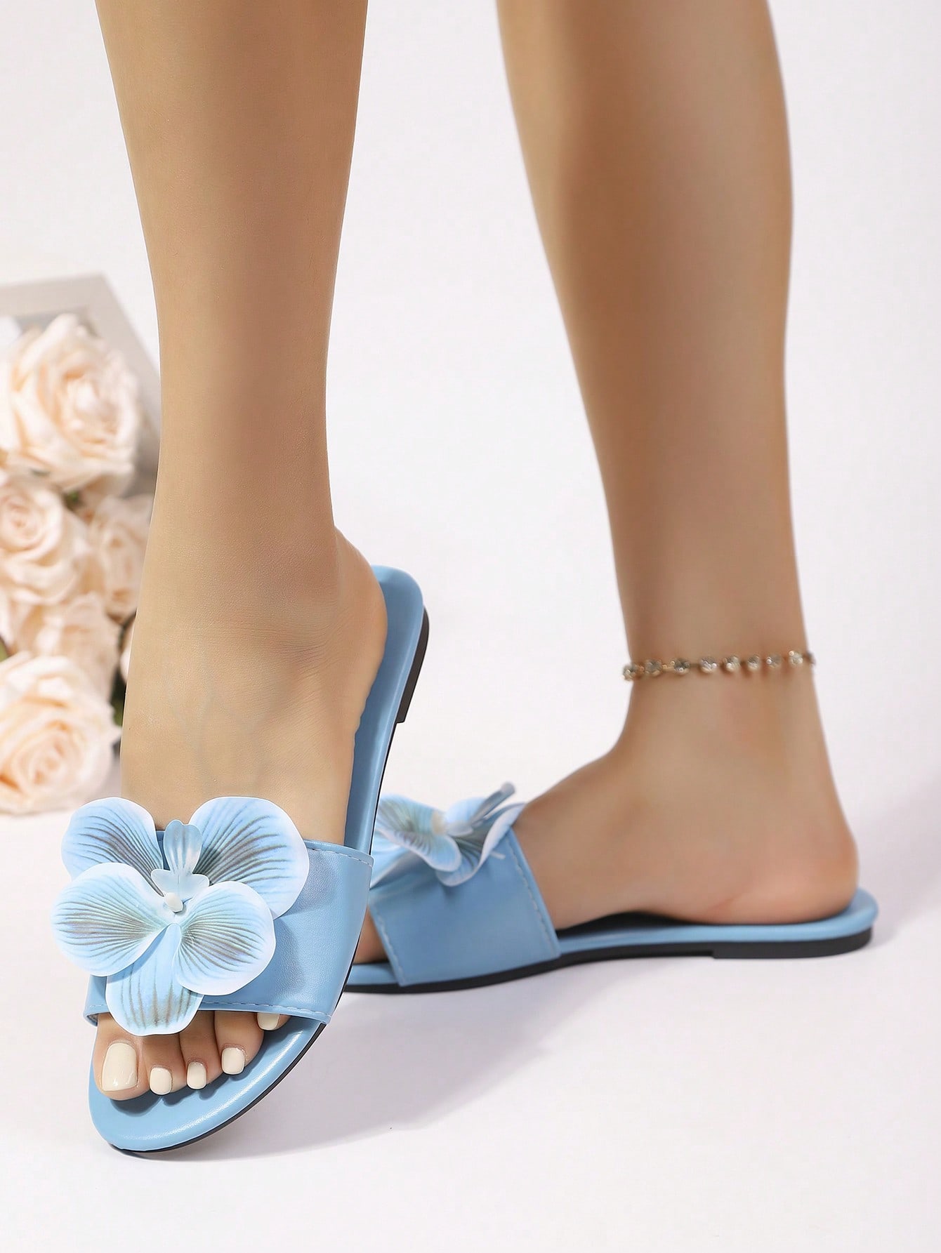 Women’s open toe flat toe-ring slide sandals with artificial flower applique detail and vacation beach style.