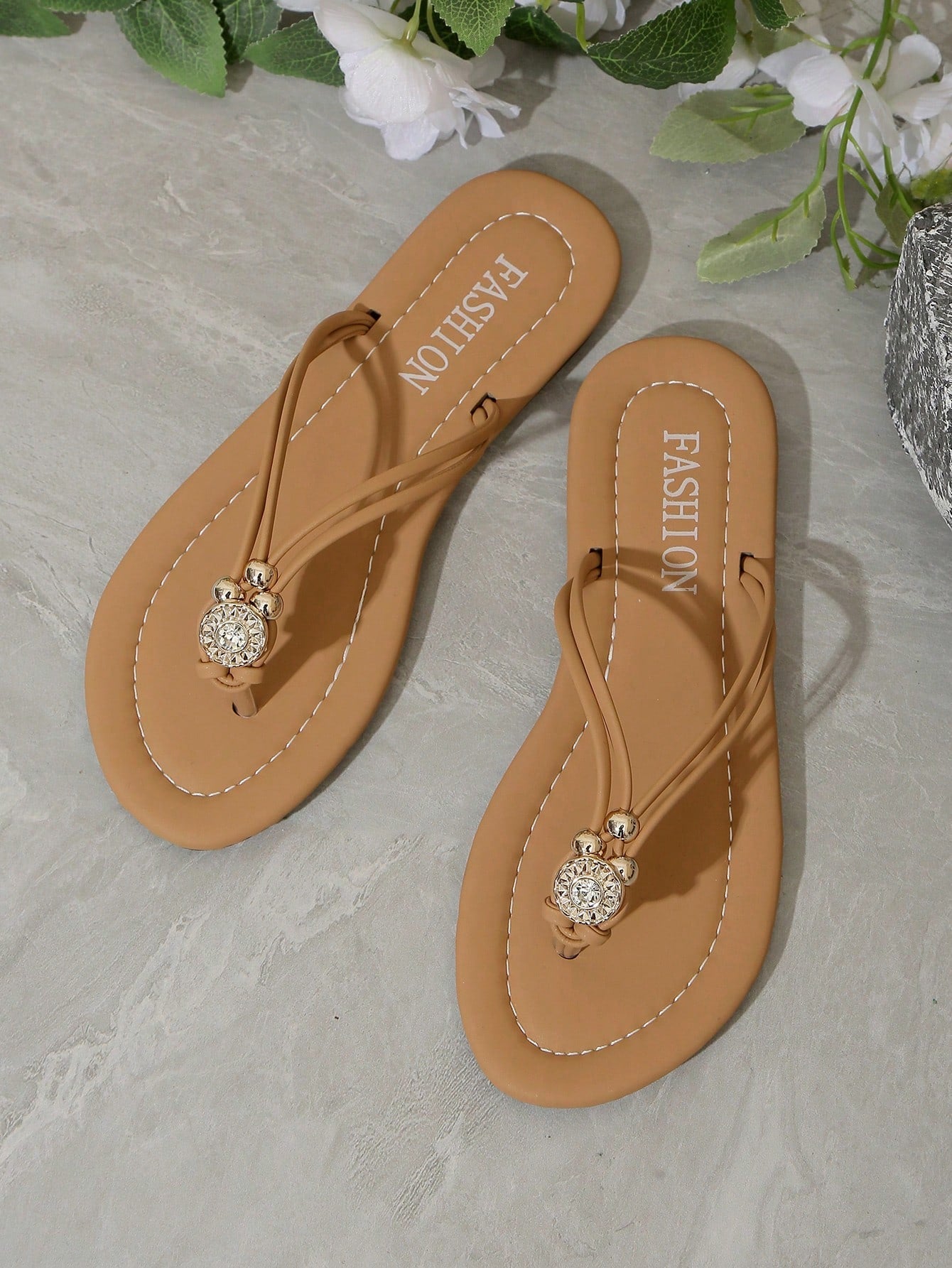 Women's brown thong flat sandals with toe post, rhinestone embellishments, beaded rope details, and metal buckle accent in a slip-on flip flop style.