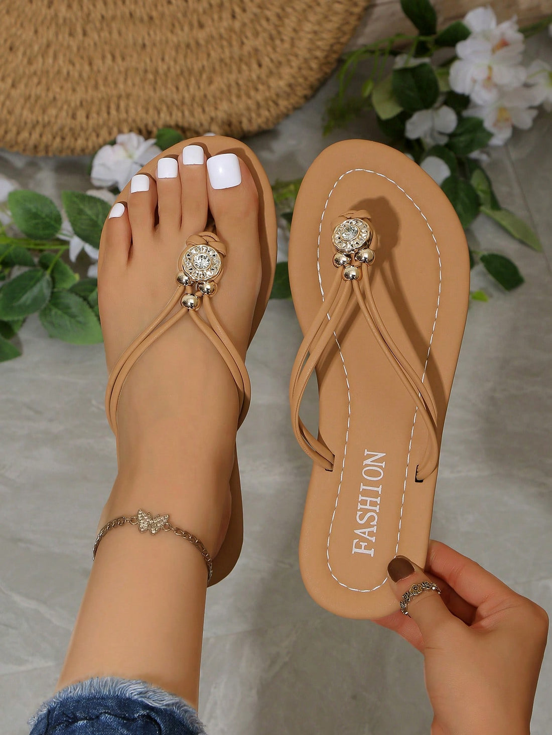 Brown women's flat thong sandals with toe post, rhinestone embellishments, beaded rope detail, and metal buckle accent in a slip-on style.
