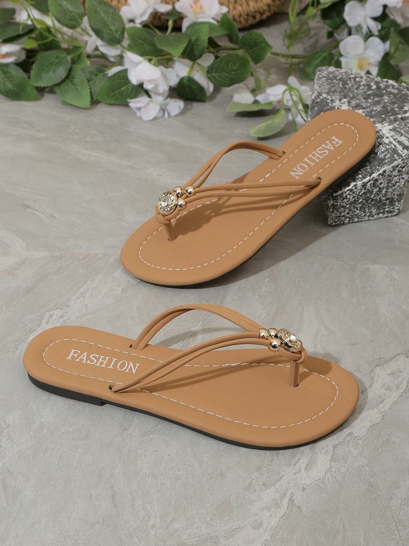 Women's brown thong flat sandals with toe post, rhinestone embellishments, beaded rope details, and metal buckle accent in a slip-on flip flop style.