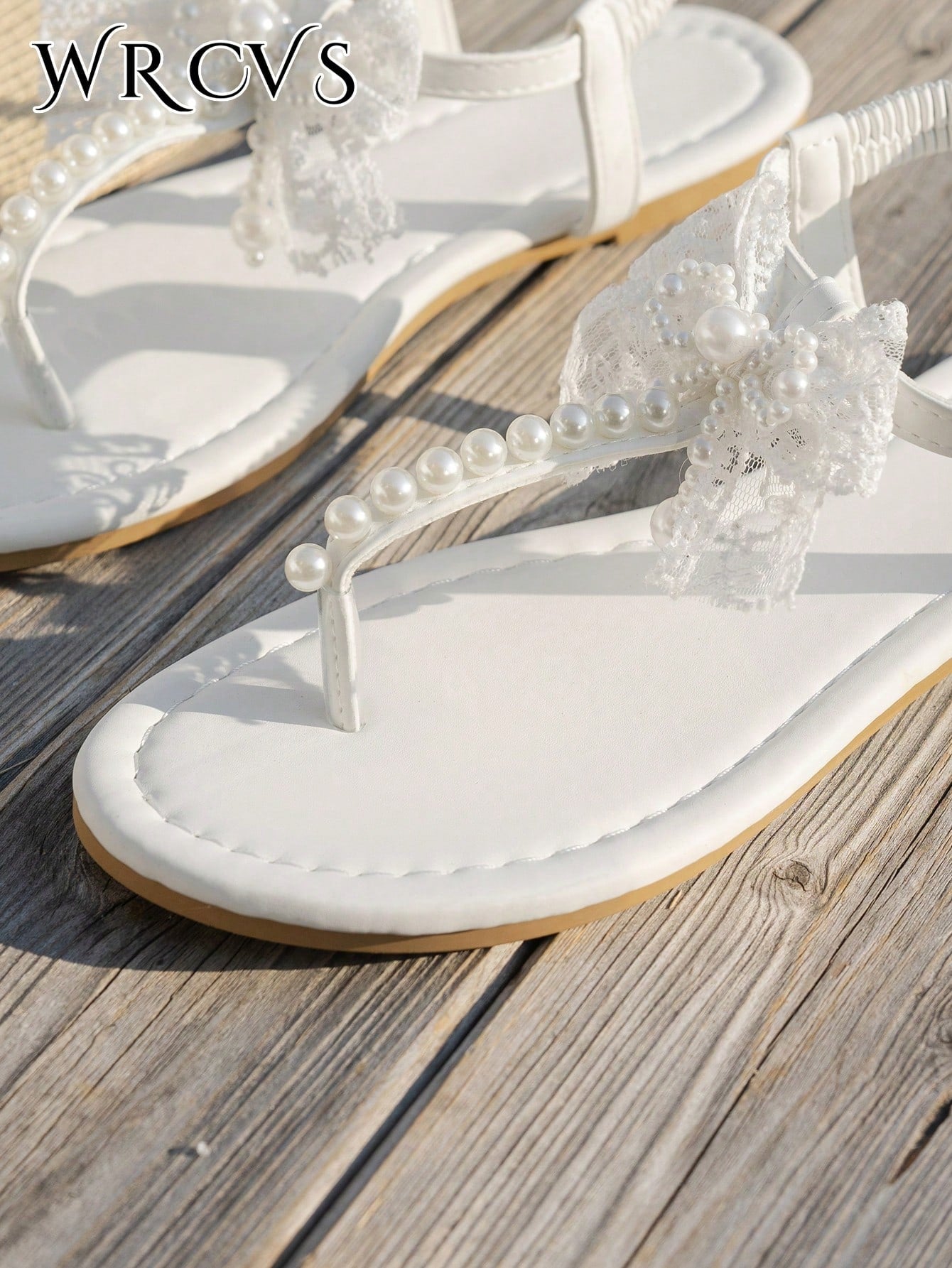 Beige women's flat thong Roman-style sandals with toe post, rhinestone and bow decoration, and buckle detail.