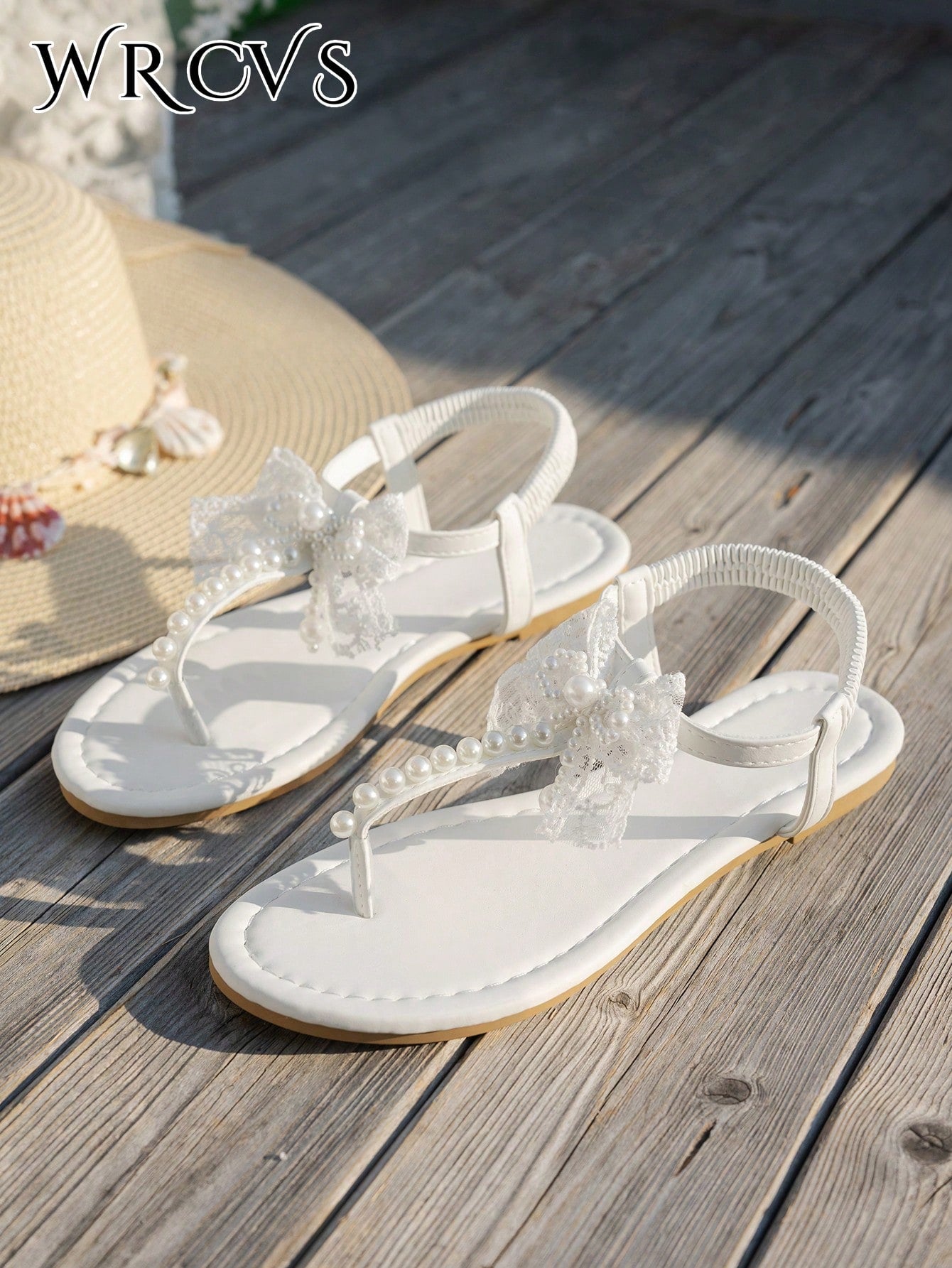 Beige women's flat thong Roman-style sandals with toe post, rhinestone and bow decoration, and buckle detail.