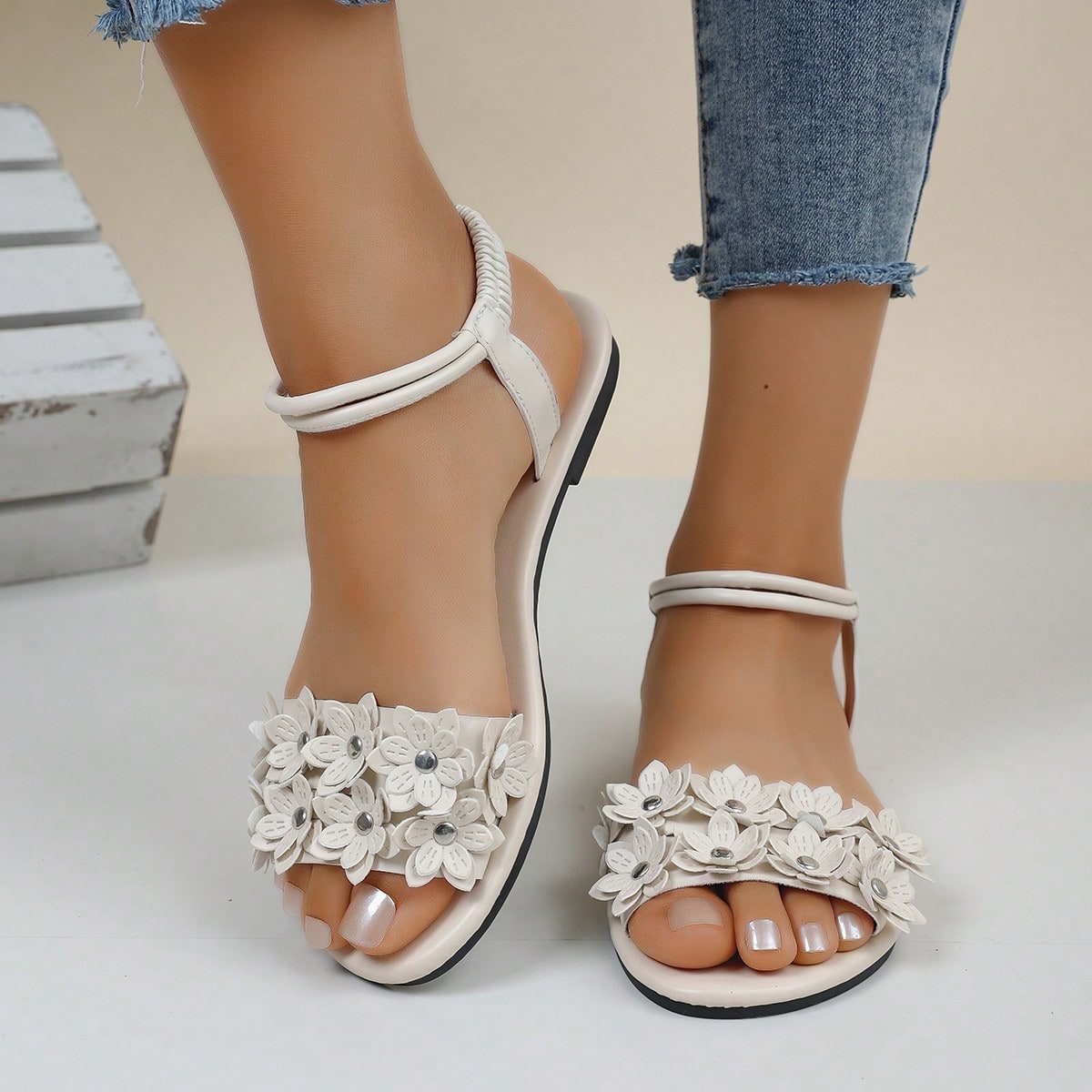 Women's beige flat sandals with stitched flower petal detail, open toe front, and adjustable ankle strap for casual warm-weather and beach wear.