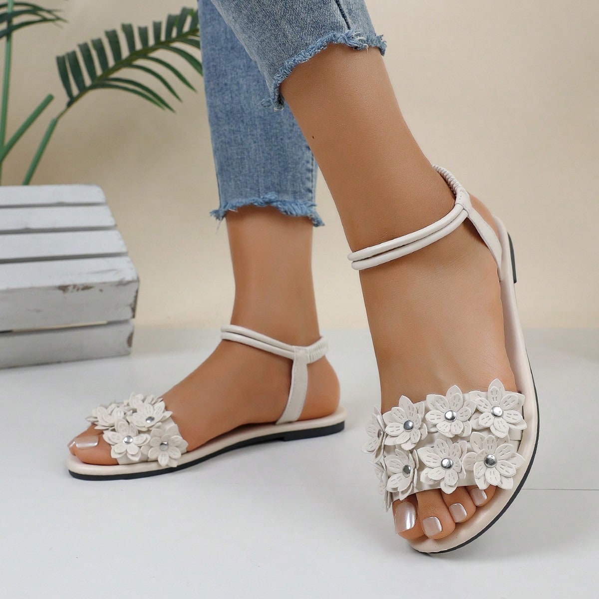 Women's beige flat sandals with stitched flower petal detail, open toe front, and adjustable ankle strap for casual warm-weather and beach wear.