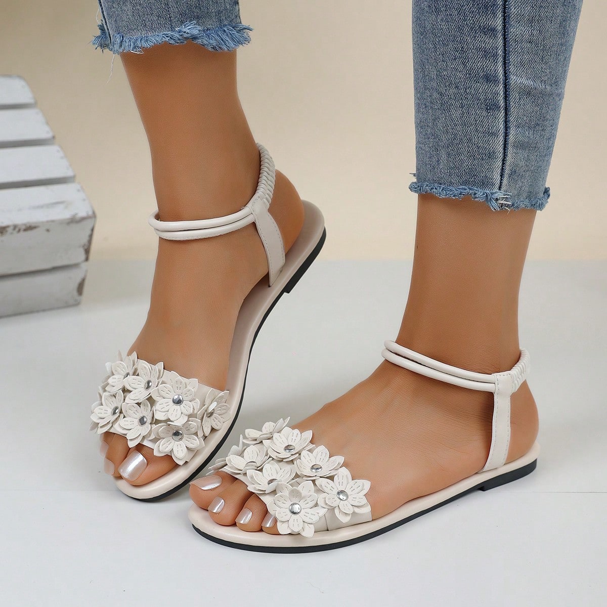 Women's beige flat sandals with stitched flower petal detail, open toe front, and adjustable ankle strap for casual warm-weather and beach wear.
