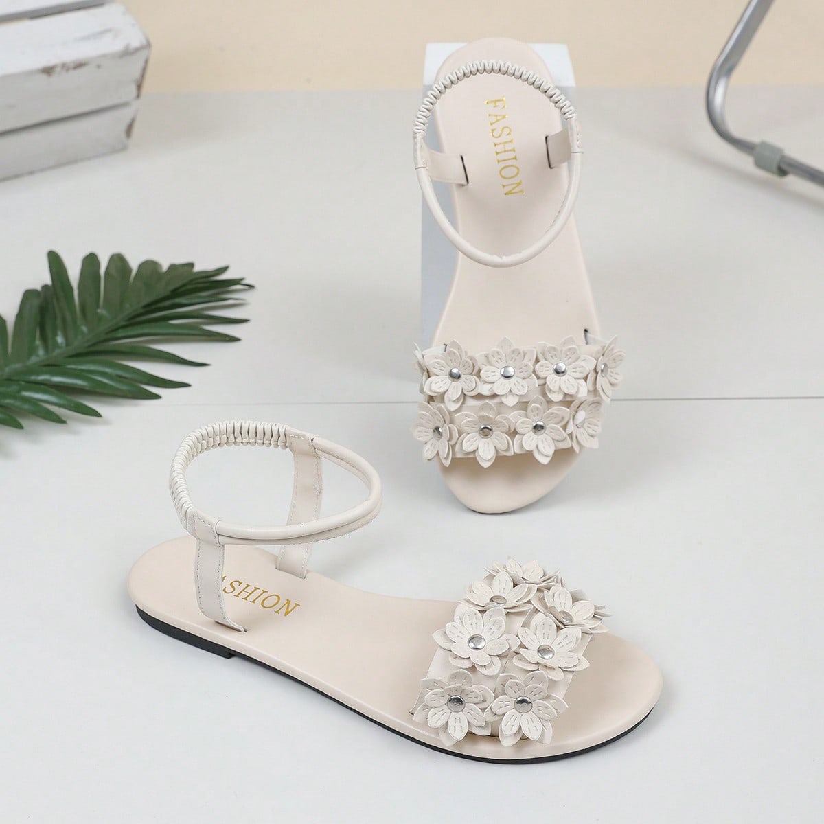 Women's beige flat sandals with stitched flower petal detail, open toe front, and adjustable ankle strap for casual warm-weather and beach wear.