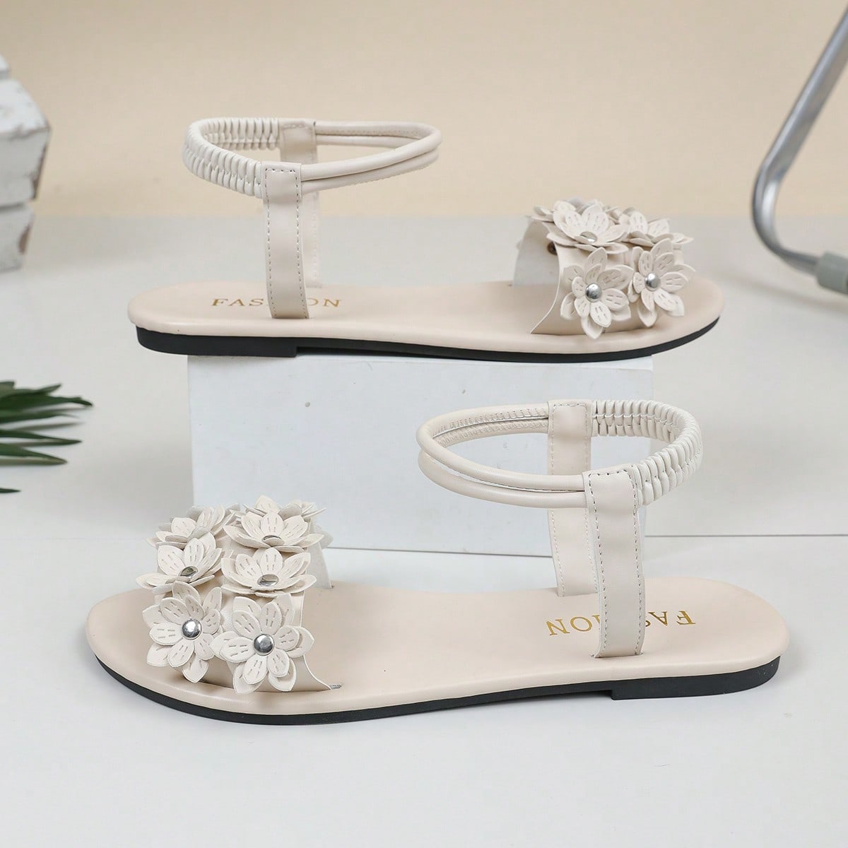 Women's beige flat sandals with stitched flower petal detail, open toe front, and adjustable ankle strap for casual warm-weather and beach wear.