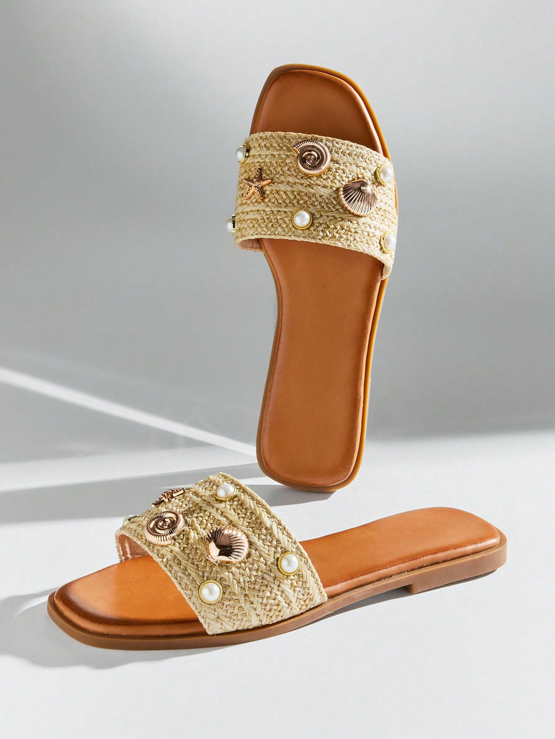 Women's slip-on flat slide sandals with open toe, woven one-band upper, and seashell and pearl ornaments in a marine life-inspired design.