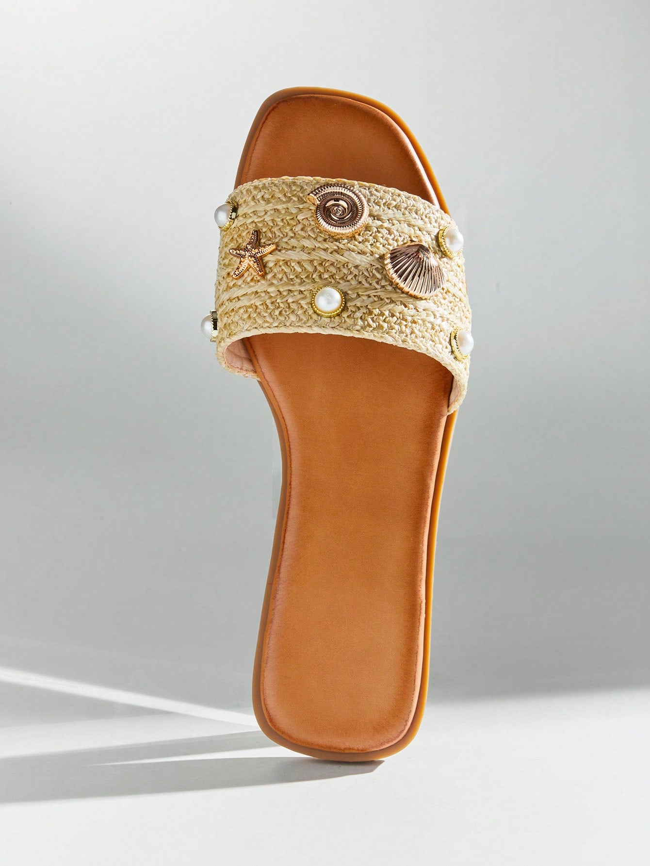 Women's slip-on flat slide sandals with open toe, woven one-band upper, and seashell and pearl ornaments in a marine life-inspired design.