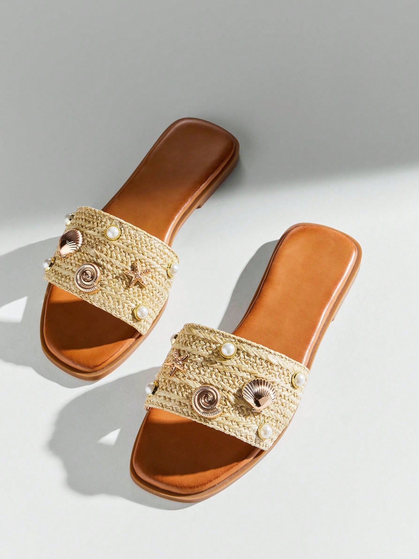 Women's slip-on flat slide sandals with open toe, woven one-band upper, and seashell and pearl ornaments in a marine life-inspired design.