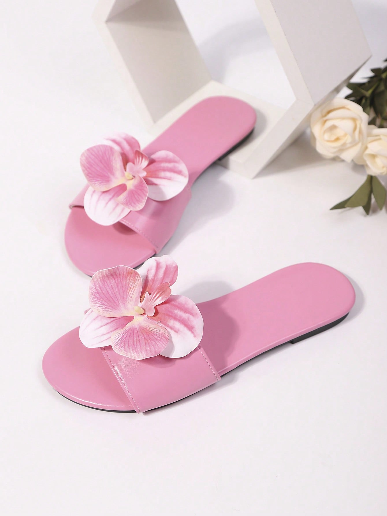 Women’s open toe flat toe-ring slide sandals with artificial flower applique detail and vacation beach style.