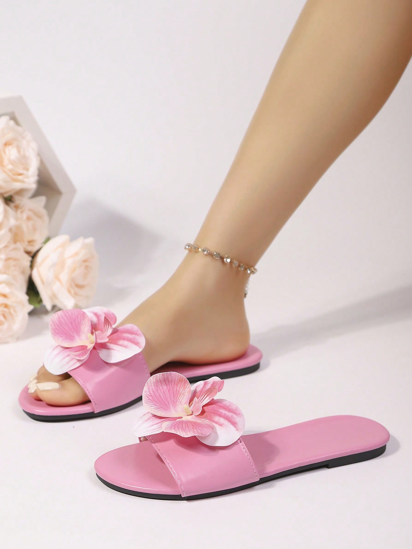 Women’s open toe flat toe-ring slide sandals with artificial flower applique detail and vacation beach style.