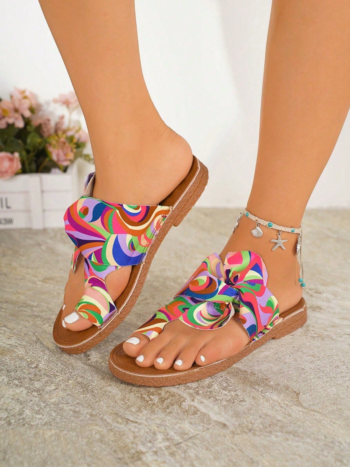 Women's flat slide sandals with bow tie, knot, and braided details, toe post design, and bohemian plant pattern.