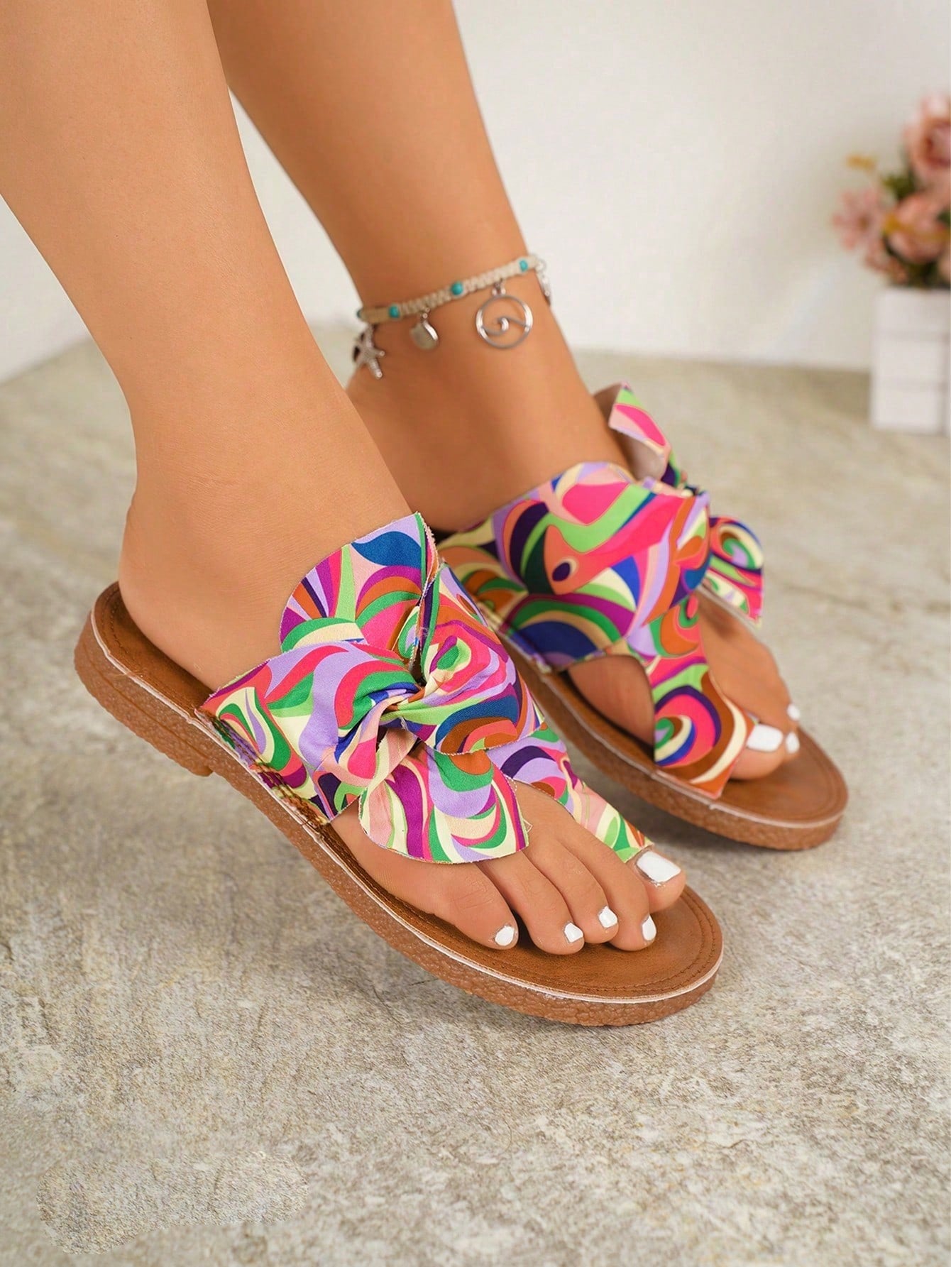 Women's flat slide sandals with bow tie, knot, and braided details, toe post design, and bohemian plant pattern.