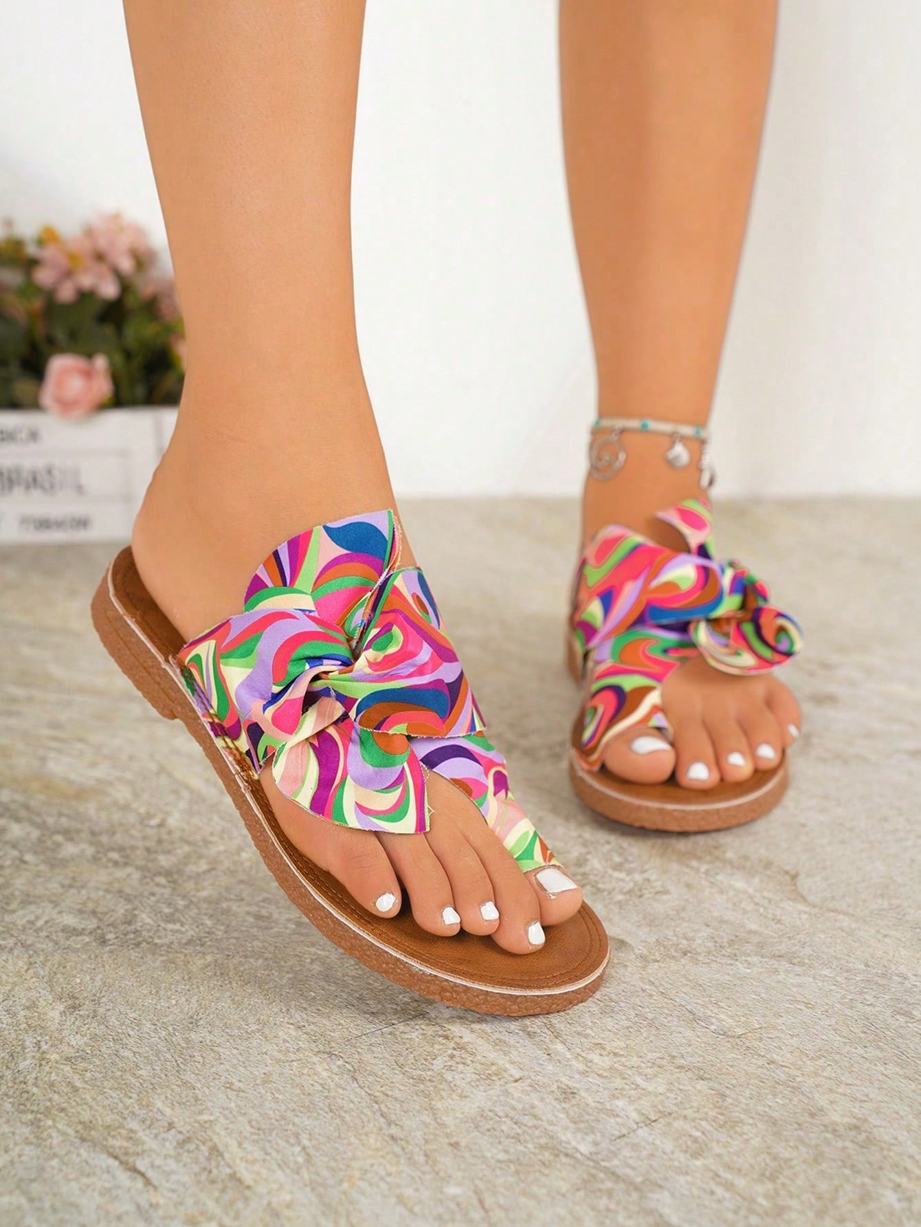 Women's flat slide sandals with bow tie, knot, and braided details, toe post design, and bohemian plant pattern.