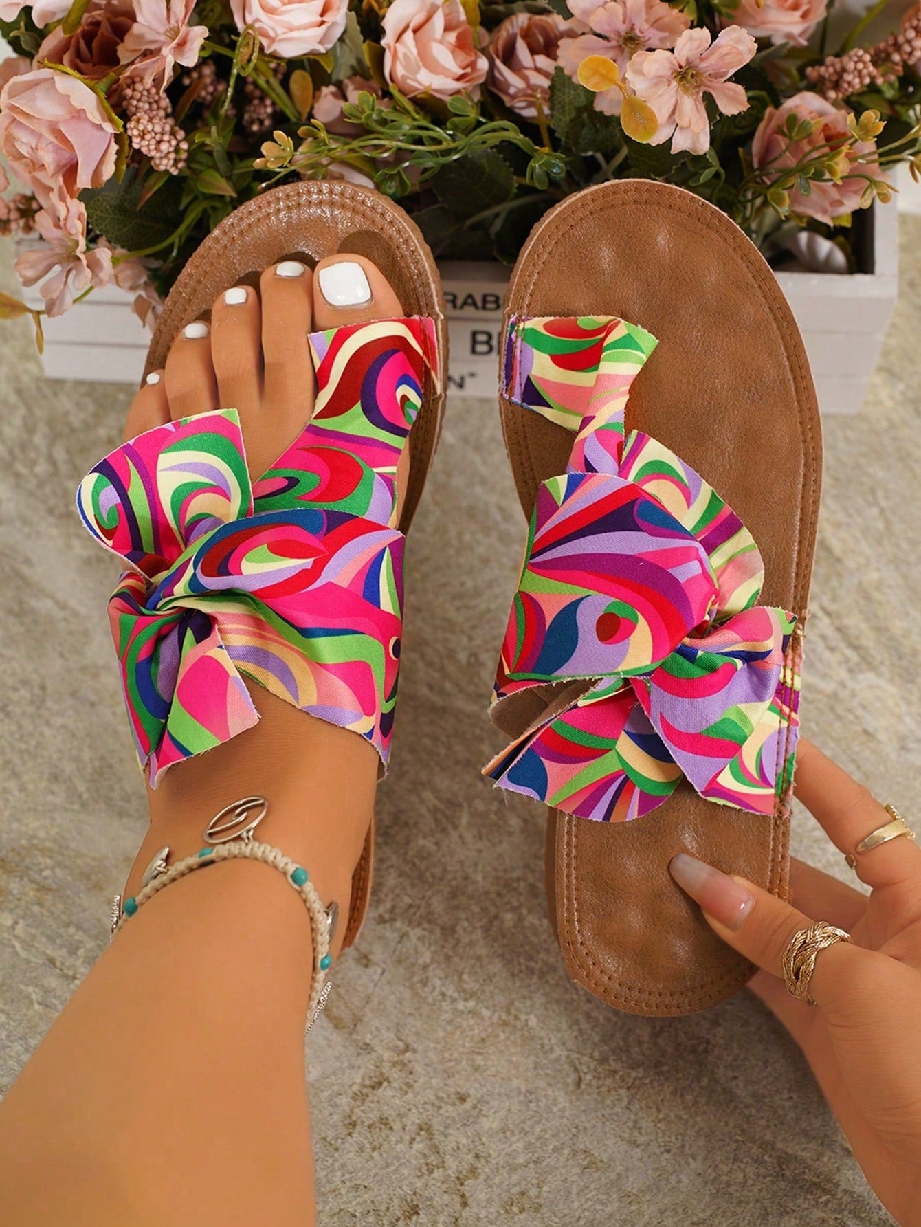Women's flat slide sandals with bow tie, knot, and braided details, toe post design, and bohemian plant pattern.