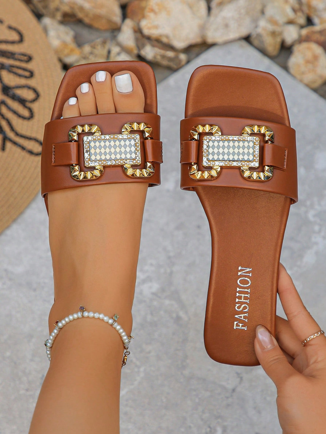 Women's one-strap flat Roman-style slide sandals with open toe, cut-out design, and rhinestone detail in brown tone.