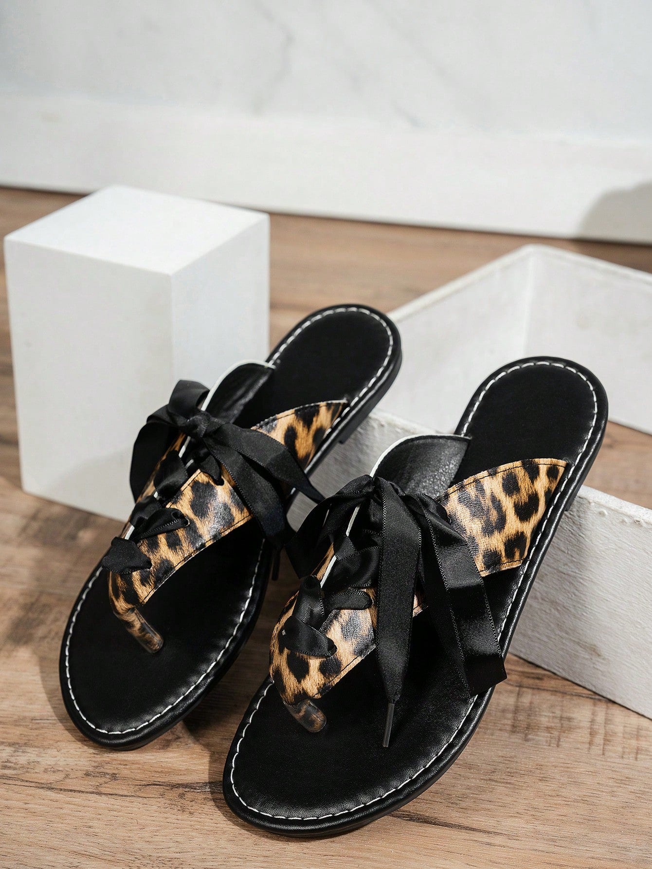 Women’s black flat toe post sandals with a leopard print satin ribbon bow, suitable for vacation, outdoor use, and everyday wear.