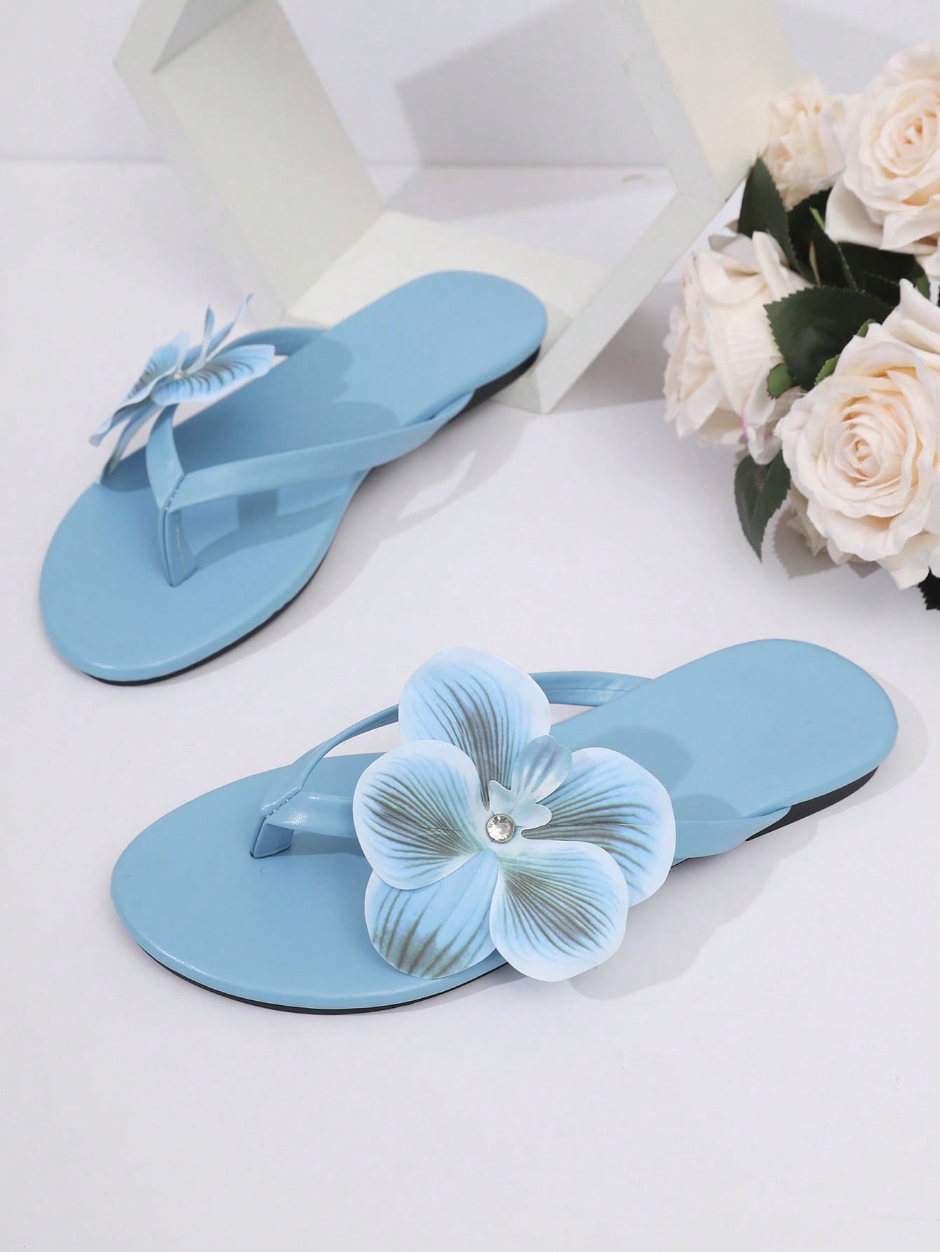 Women’s open toe flat toe-ring slide sandals with artificial flower applique detail and vacation beach style.