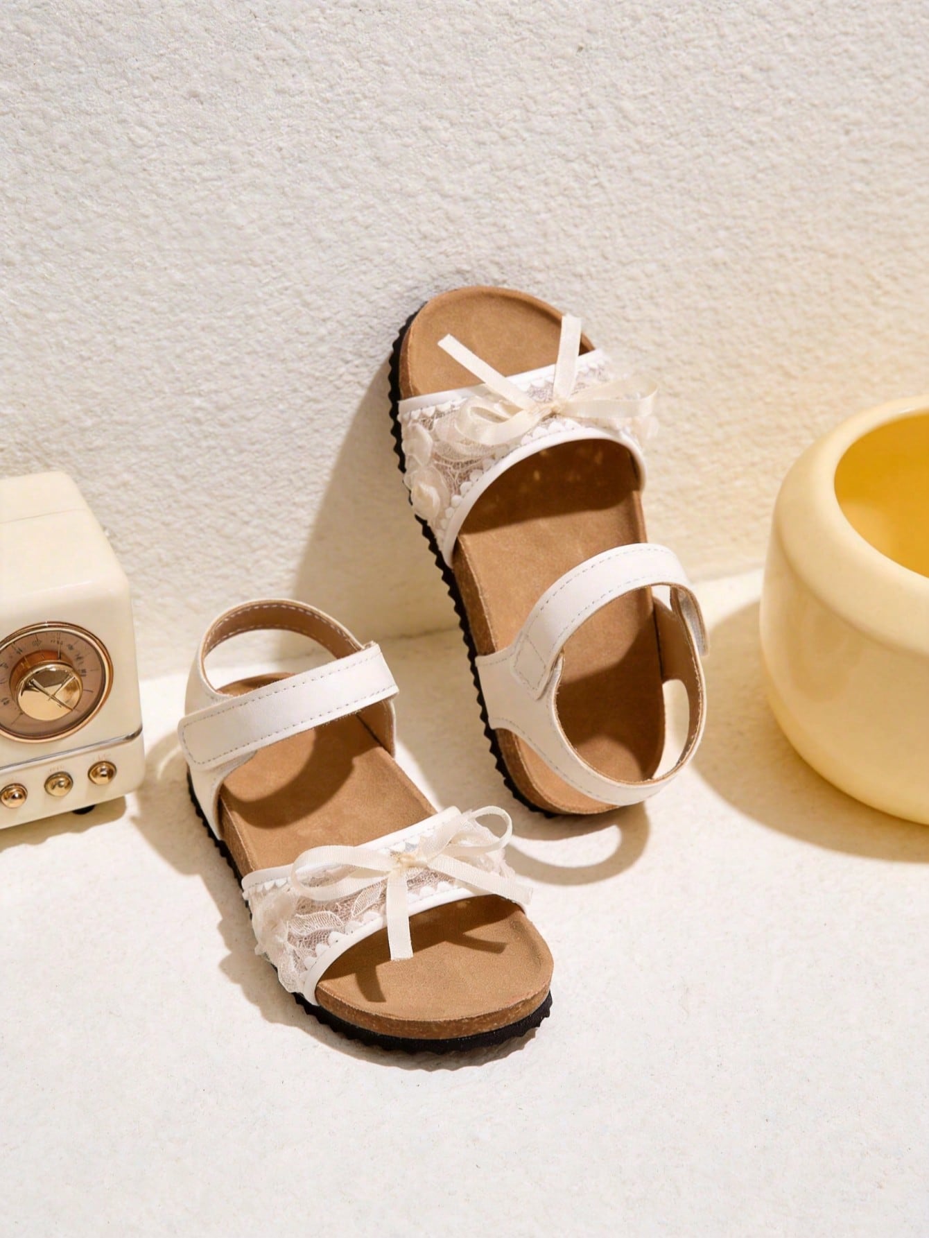 Pair of girls' pink open-toe flat sandals with ankle straps, buckle details, and a non-slip black rubber outsole.
