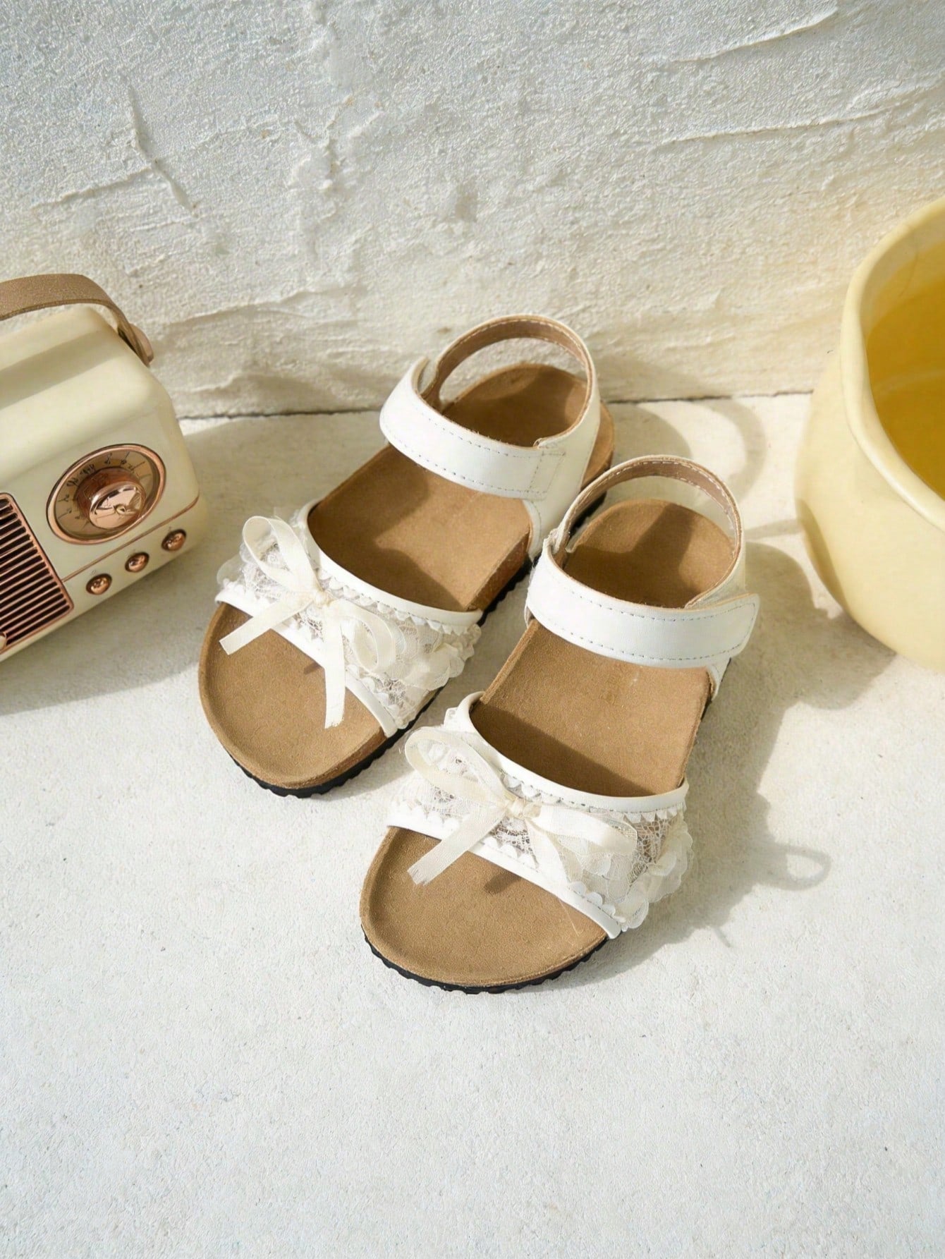 Pair of girls' pink open-toe flat sandals with ankle straps, buckle details, and a non-slip black rubber outsole.