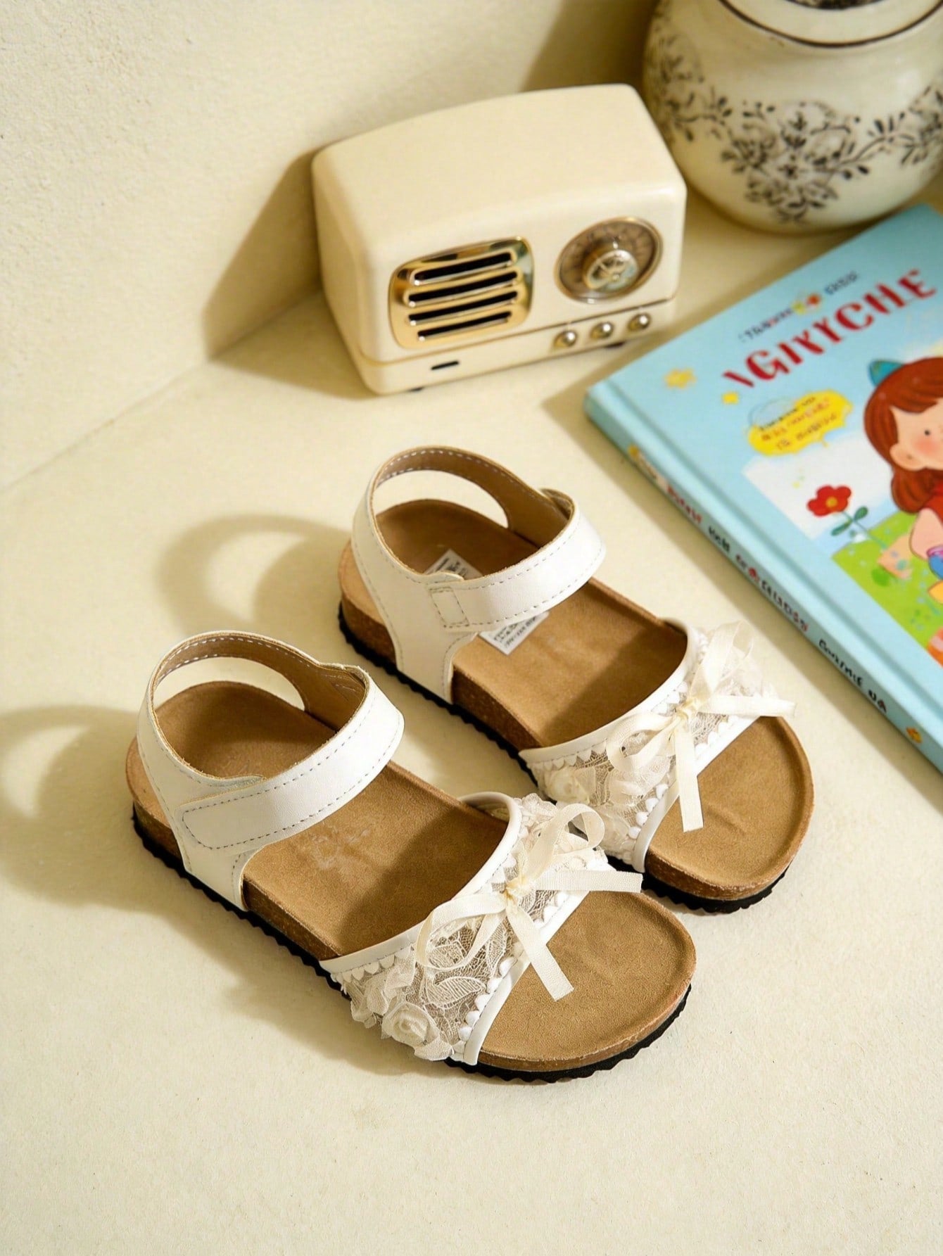 Pair of girls' pink open-toe flat sandals with ankle straps, buckle details, and a non-slip black rubber outsole.