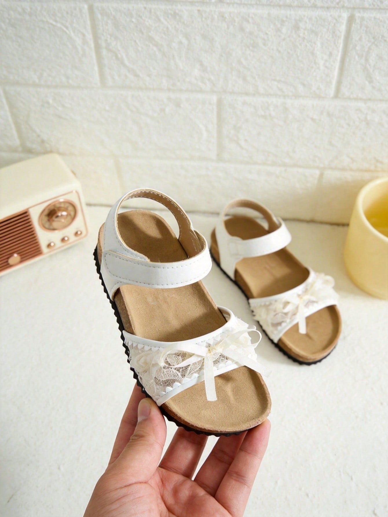 Pair of girls' pink open-toe flat sandals with ankle straps, buckle details, and a non-slip black rubber outsole.