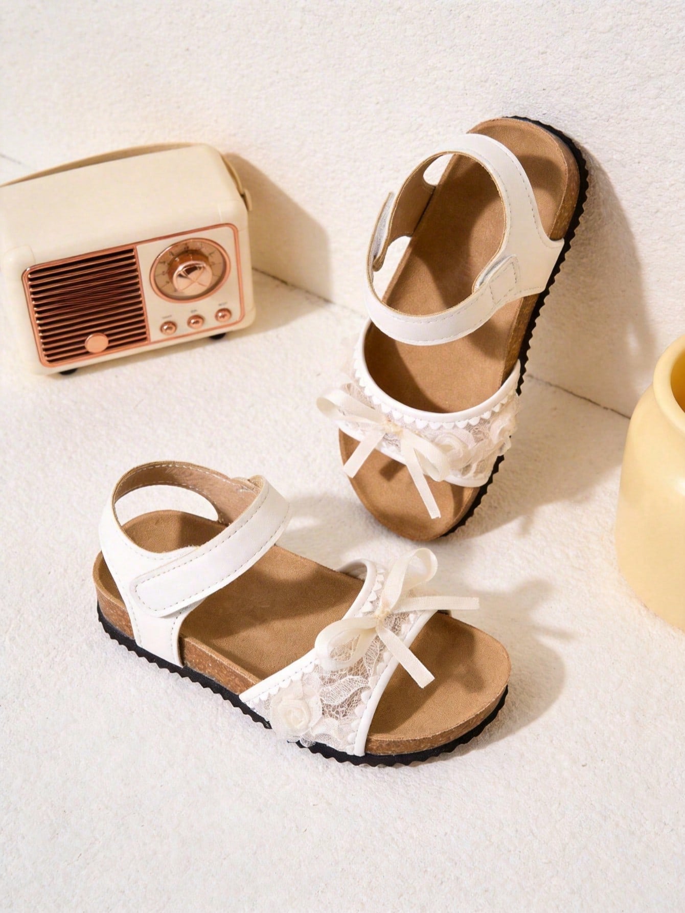 Pair of girls' pink open-toe flat sandals with ankle straps, buckle details, and a non-slip black rubber outsole.