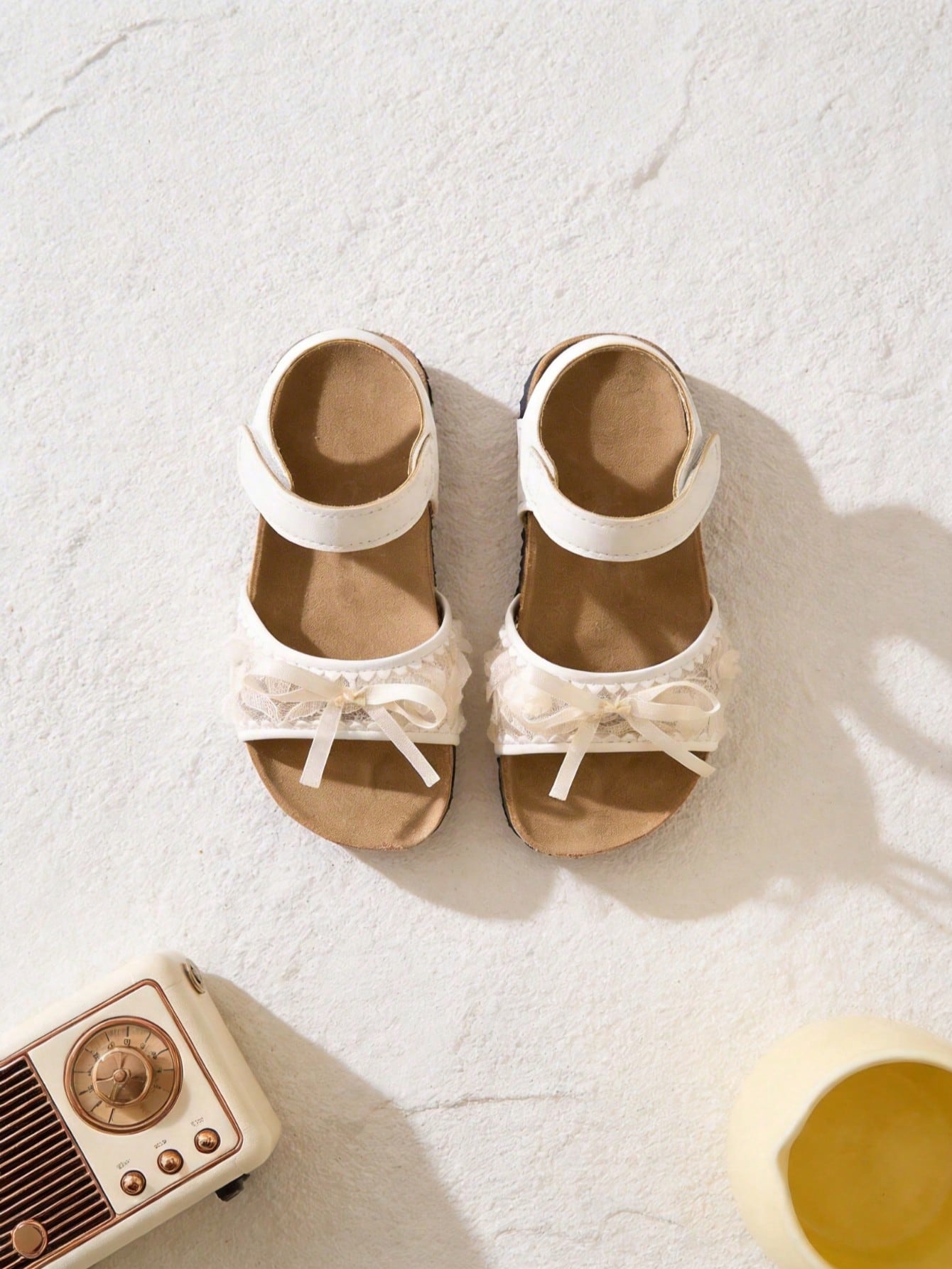Pair of girls' pink open-toe flat sandals with ankle straps, buckle details, and a non-slip black rubber outsole.