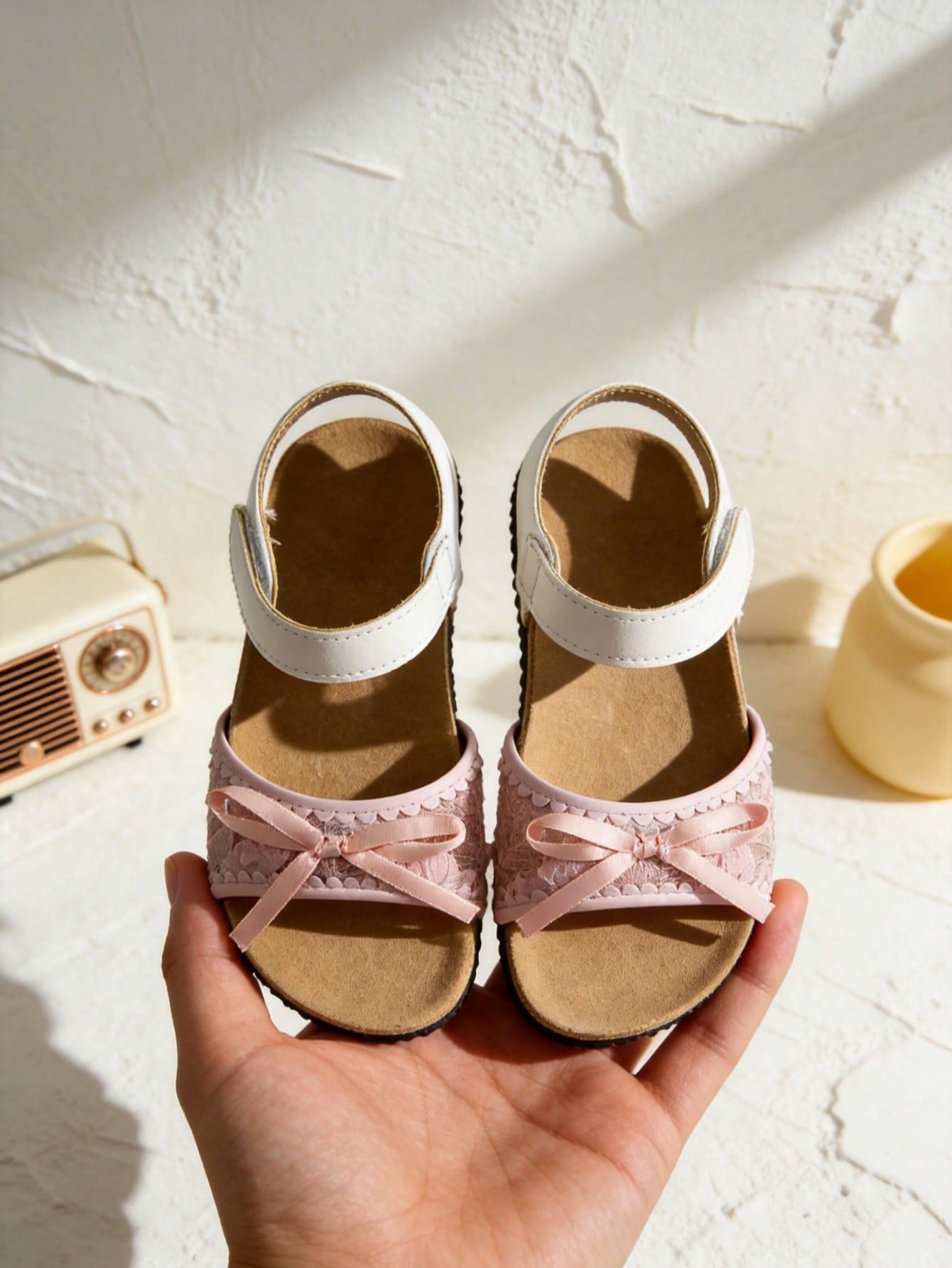 Pair of girls' pink open-toe flat sandals with ankle straps, buckle details, and a non-slip black rubber outsole.