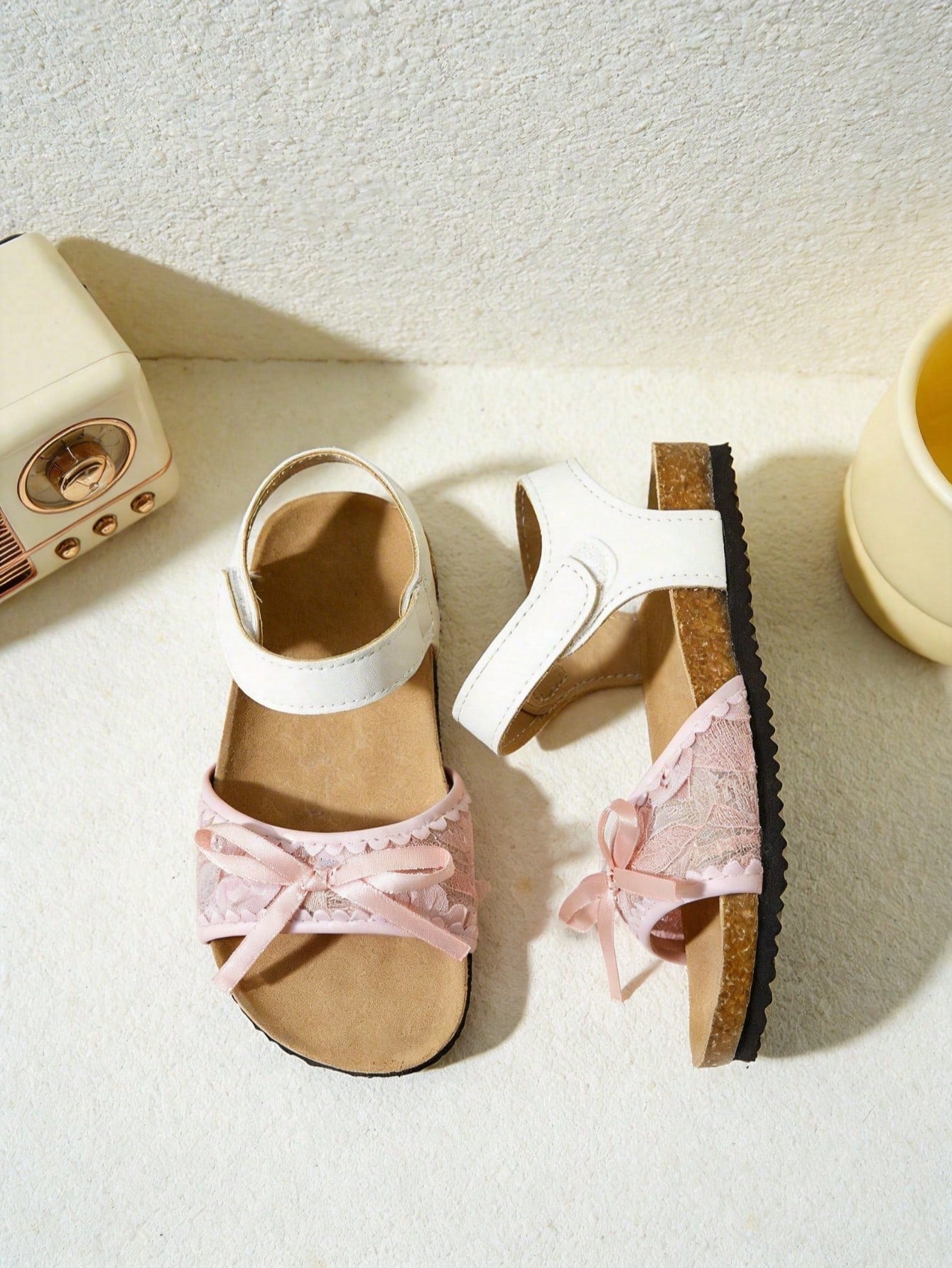 Pair of girls' pink open-toe flat sandals with ankle straps, buckle details, and a non-slip black rubber outsole.