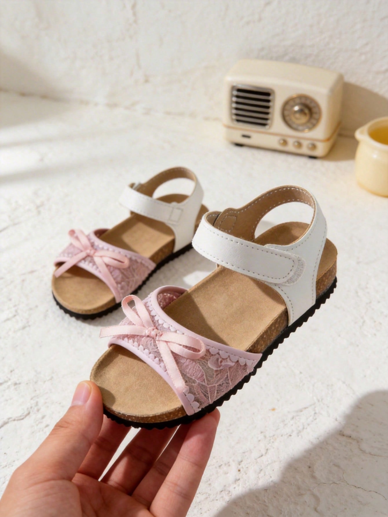 Pair of girls' pink open-toe flat sandals with ankle straps, buckle details, and a non-slip black rubber outsole.