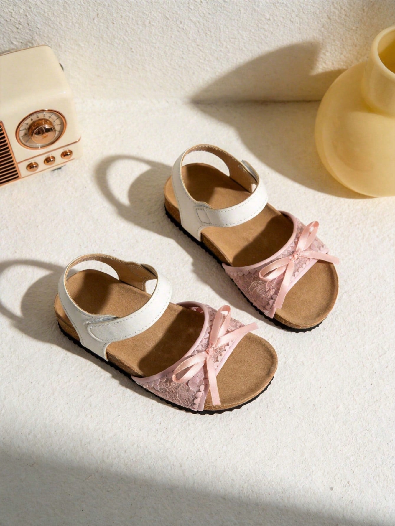 Pair of girls' pink open-toe flat sandals with ankle straps, buckle details, and a non-slip black rubber outsole.
