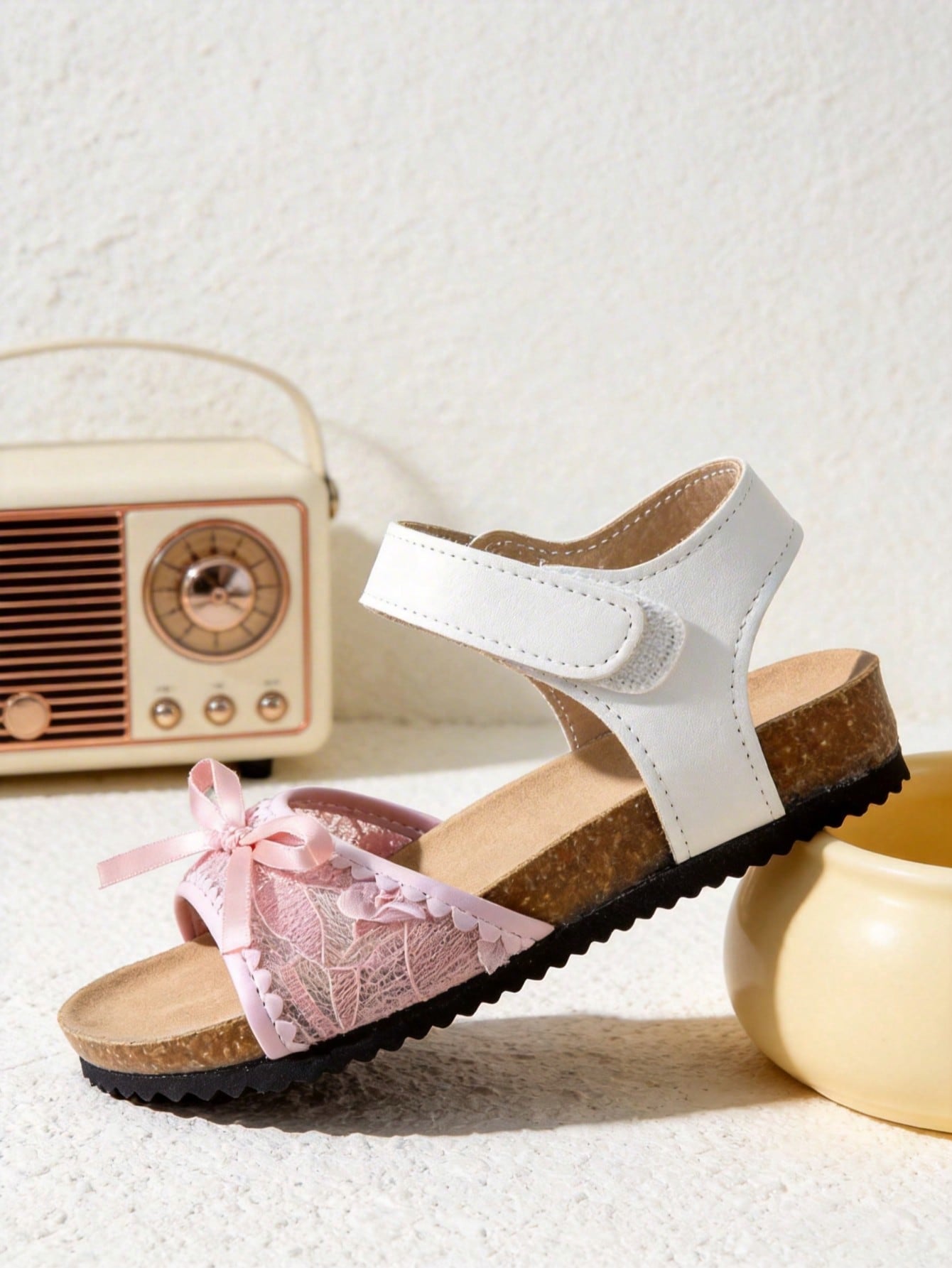 Pair of girls' pink open-toe flat sandals with ankle straps, buckle details, and a non-slip black rubber outsole.
