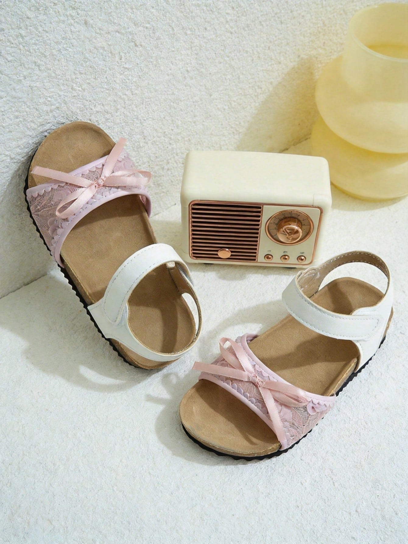 Pair of girls' pink open-toe flat sandals with ankle straps, buckle details, and a non-slip black rubber outsole.