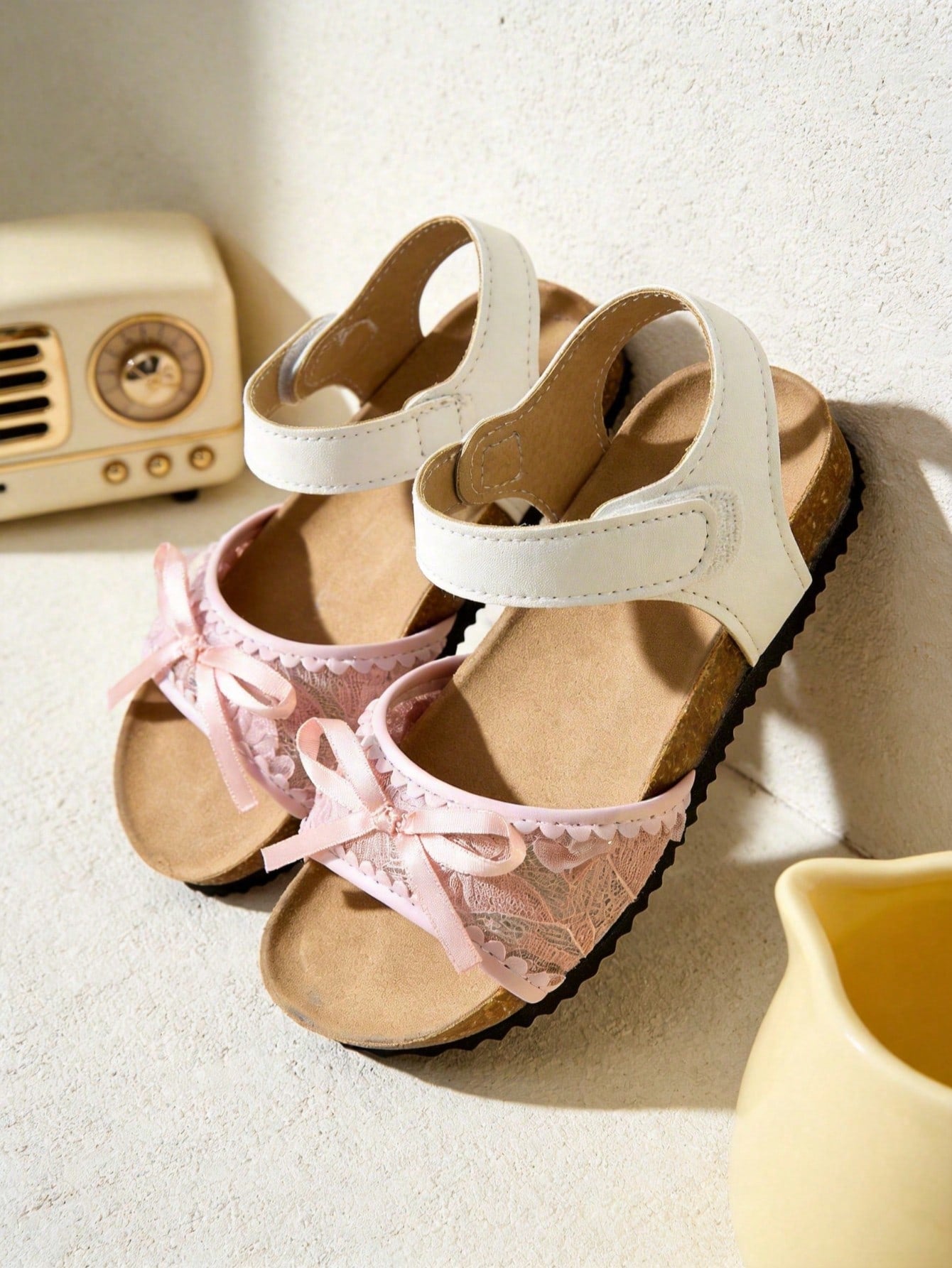 Pair of girls' pink open-toe flat sandals with ankle straps, buckle details, and a non-slip black rubber outsole.
