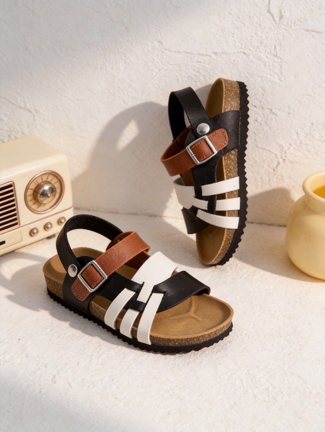 Pair of girls' pink open-toe flat sandals with ankle straps, buckle details, and a non-slip black rubber outsole.