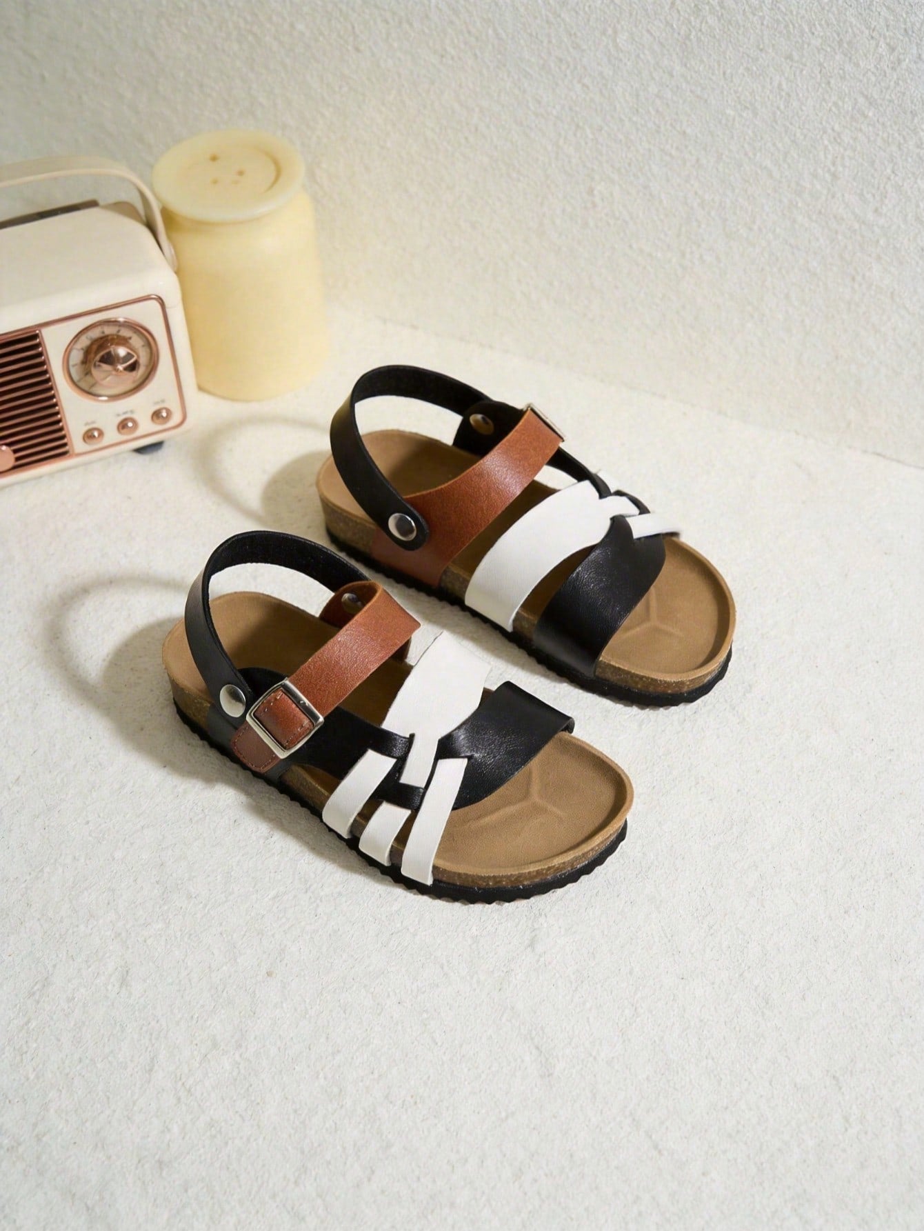 Pair of girls' pink open-toe flat sandals with ankle straps, buckle details, and a non-slip black rubber outsole.