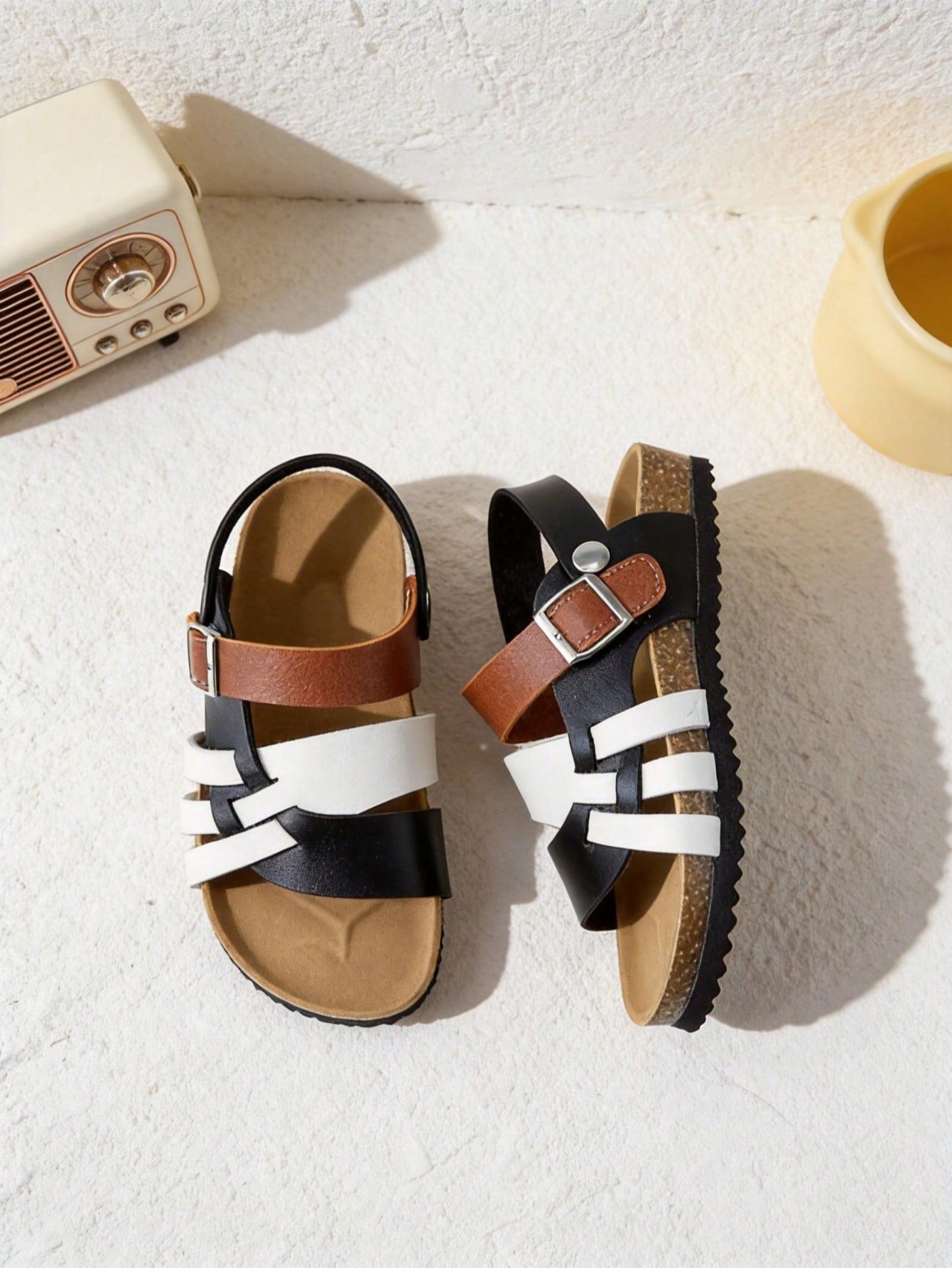 Pair of girls' pink open-toe flat sandals with ankle straps, buckle details, and a non-slip black rubber outsole.