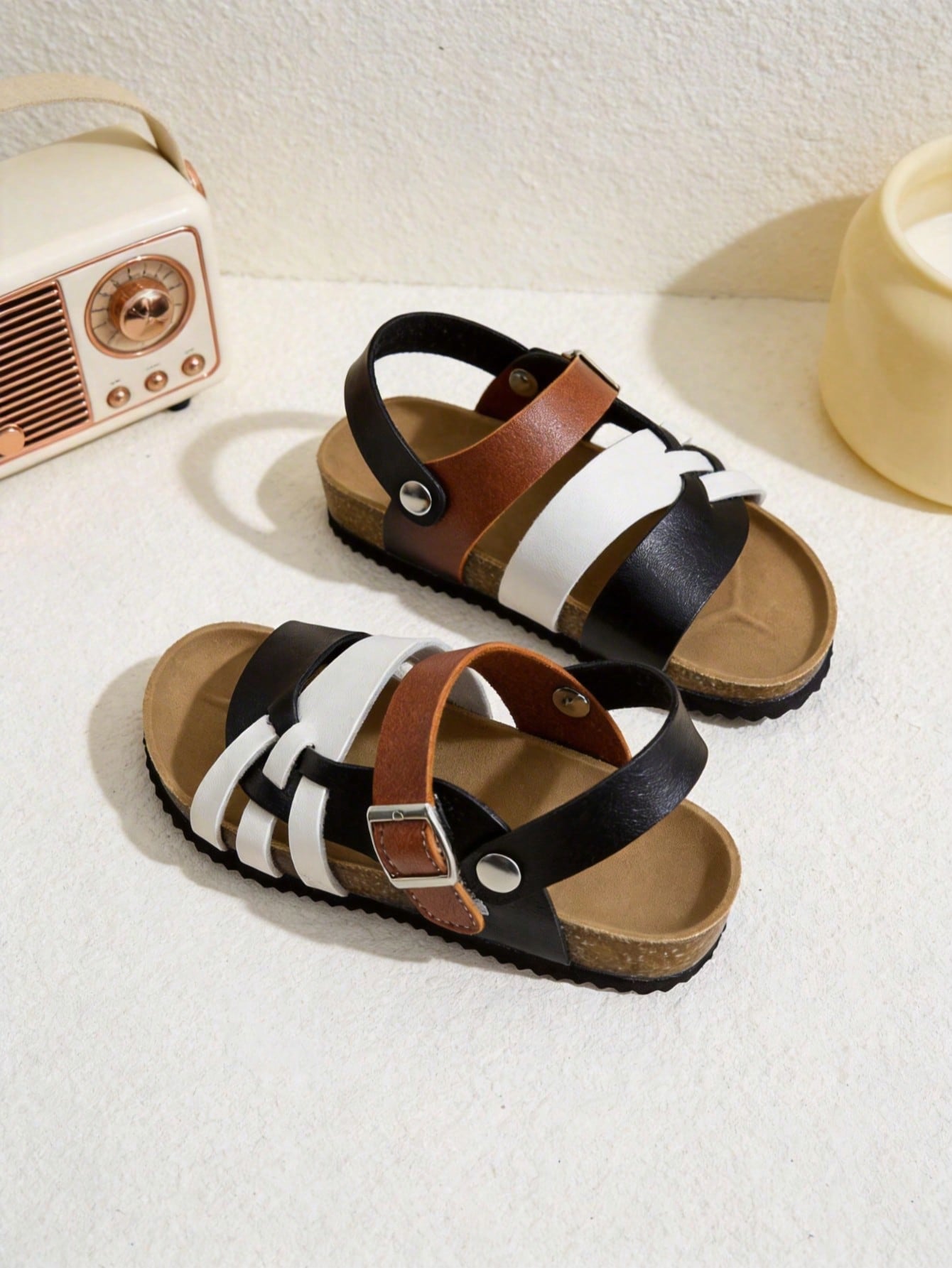 Pair of girls' pink open-toe flat sandals with ankle straps, buckle details, and a non-slip black rubber outsole.